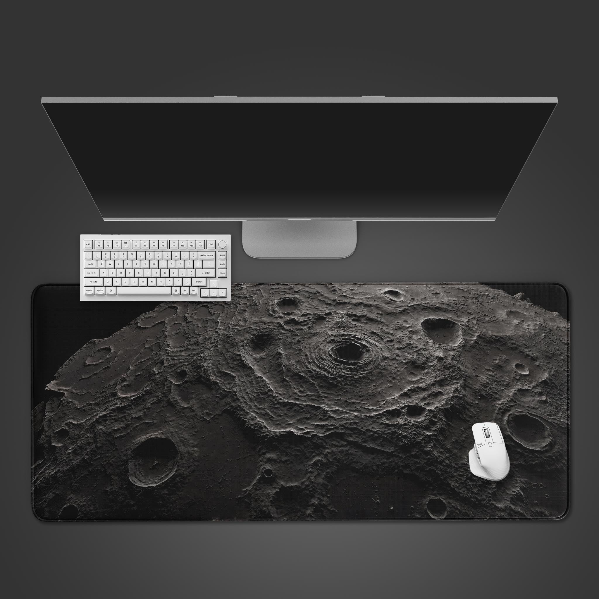 Desk setup with a computer monitor, keyboard, mouse, and mouse pad featuring a lunar surface design on a black background.