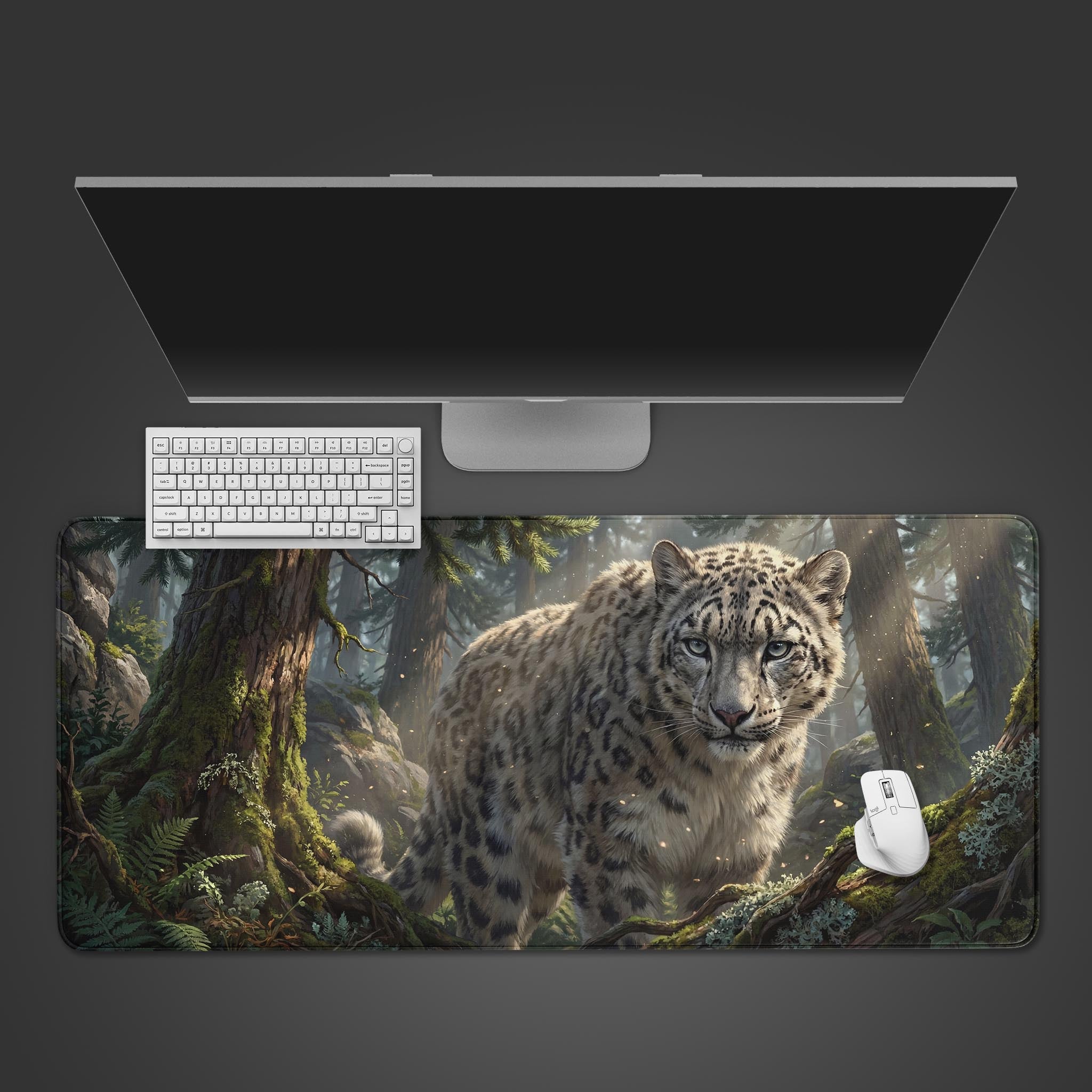 Top-down view of the Alpine Ghost Sentinel gaming desk mat, featuring a snow leopard in a forest, shown with a white keyboard, mouse, and a large monitor on a gray surface. - Epic Design Pads & Mousepads