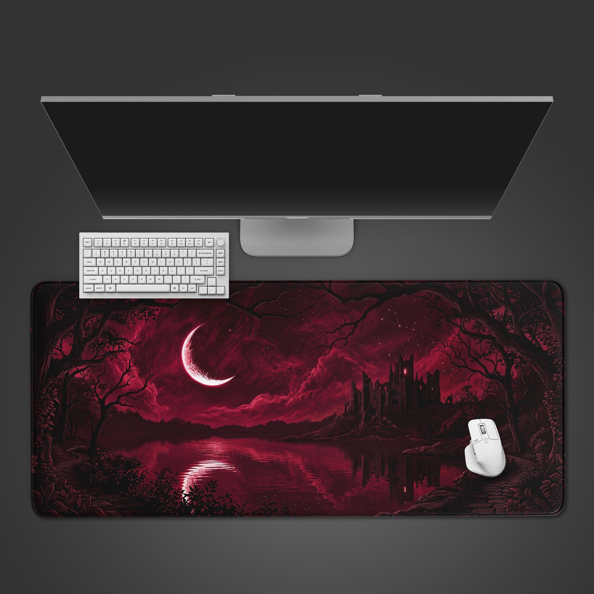 The Blood Moon Keep gaming desk mat displayed on a dark surface, with a white keyboard and mouse positioned on it, beneath a large monitor. - Epic Design Pads & Mousepads