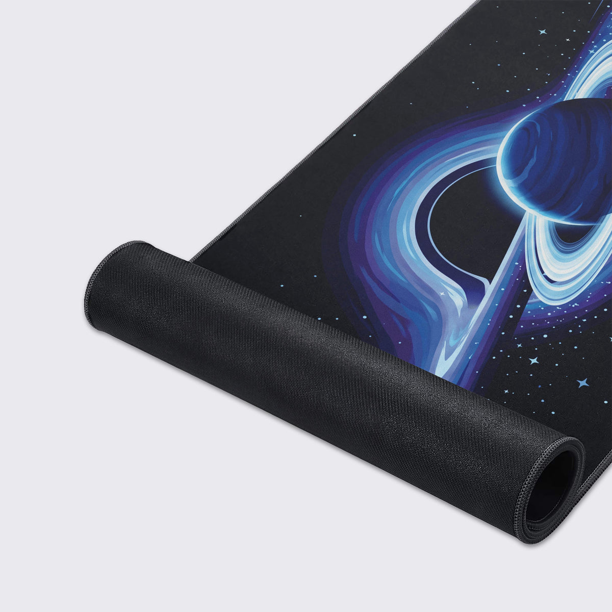 Partly rolled desk mat showing its black non-slip rubber underside and the blue ringed planet and black hole art.