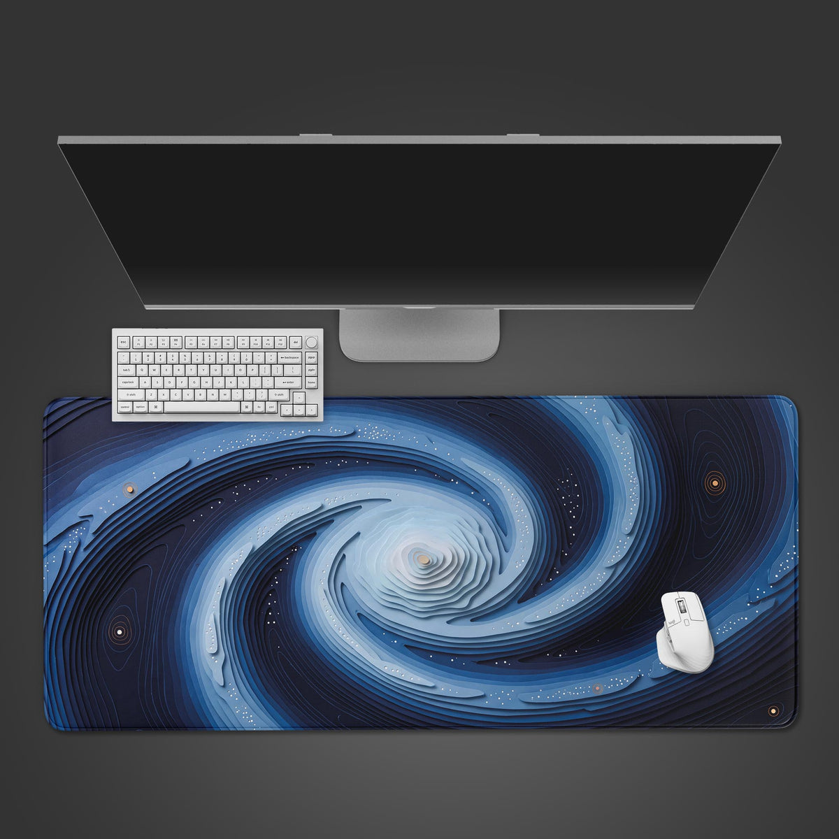 Blue galaxy abstract desk mat from above, layered spiral art under a silver monitor, white keyboard and mouse