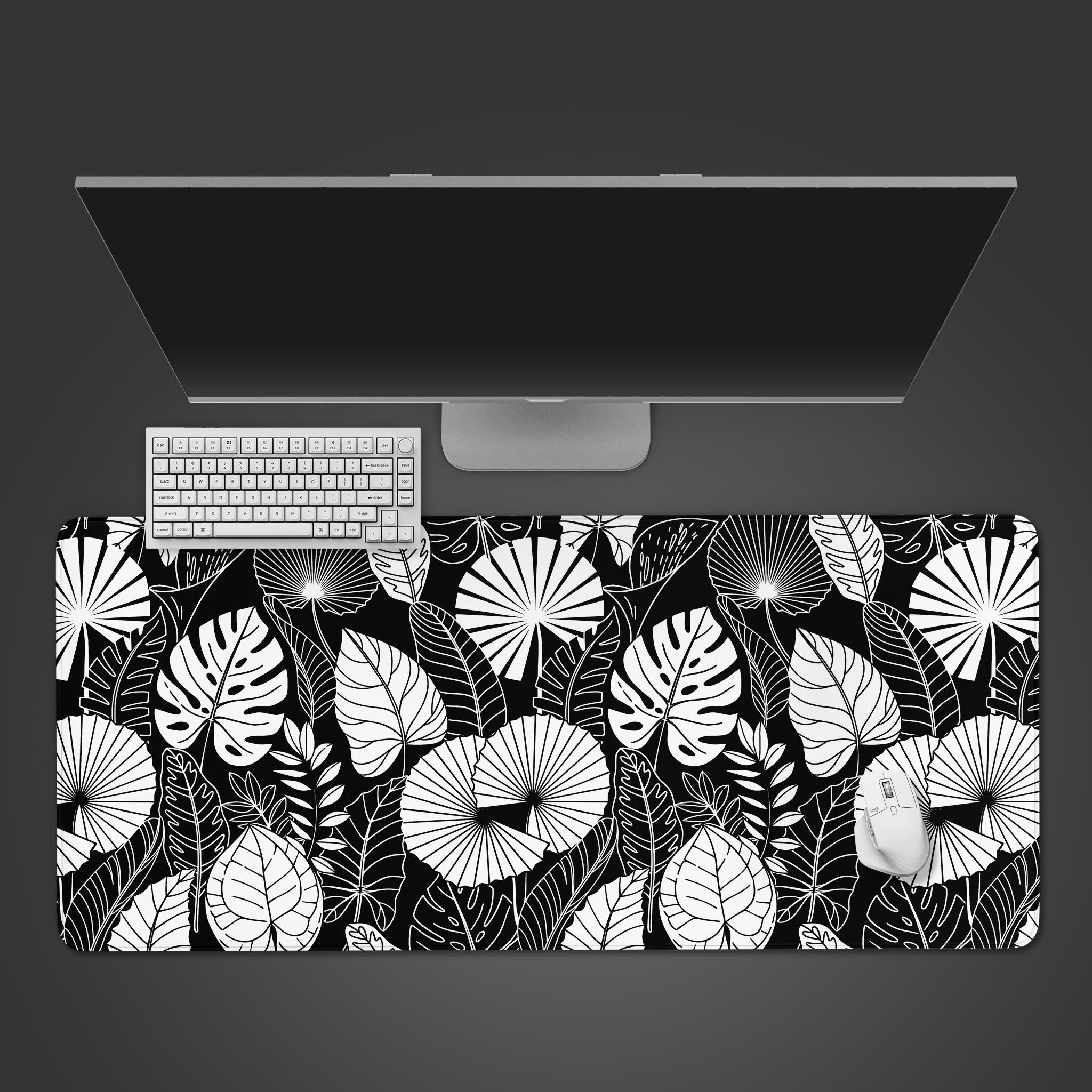 Botanical Black desk mat with a tropical leaf pattern, shown in a top-down desktop view with a white keyboard and mouse. - Epic Design Pads
