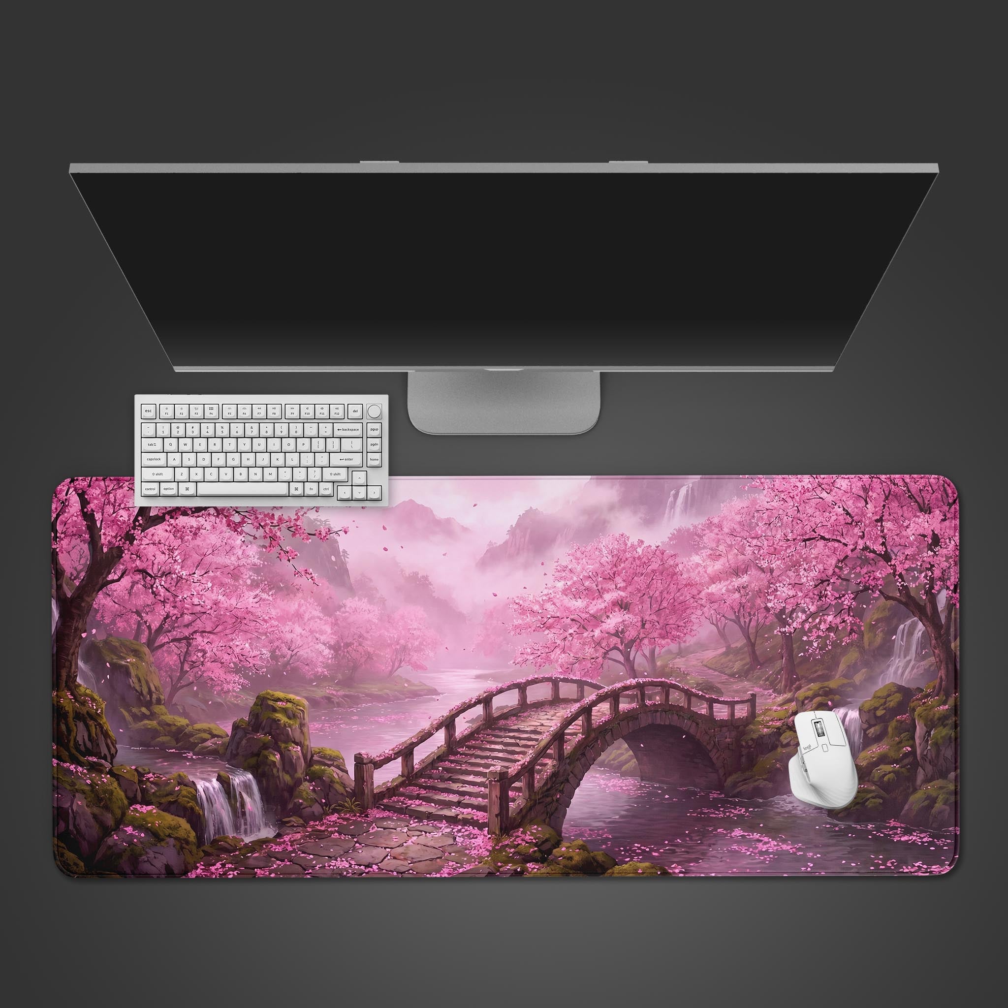 A pink cherry blossom desk mat featuring a wooden bridge over a tranquil river with waterfalls and misty mountains.