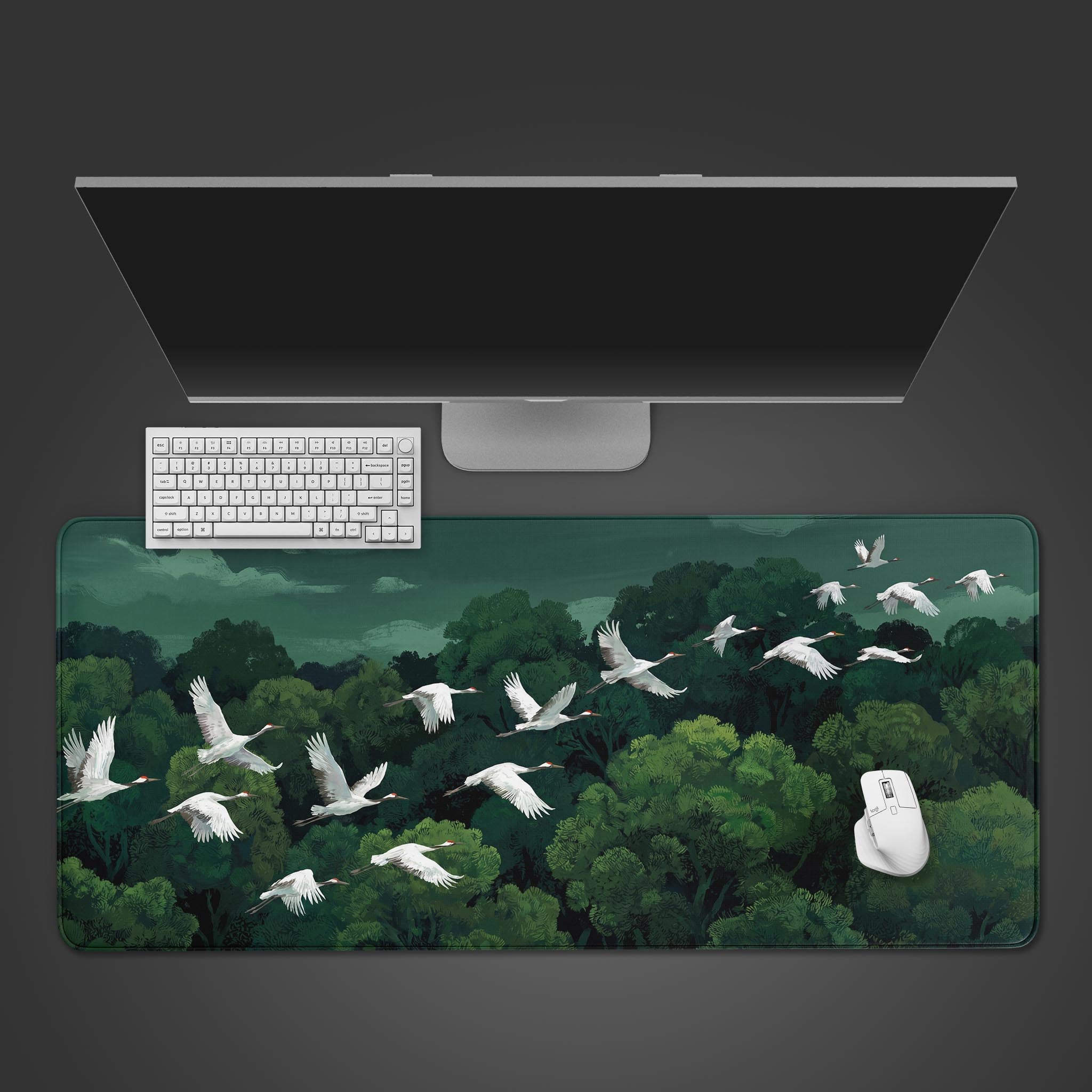 A serene desk mat featuring a flock of white red-crowned cranes flying over a dense green forest under a grey sky.