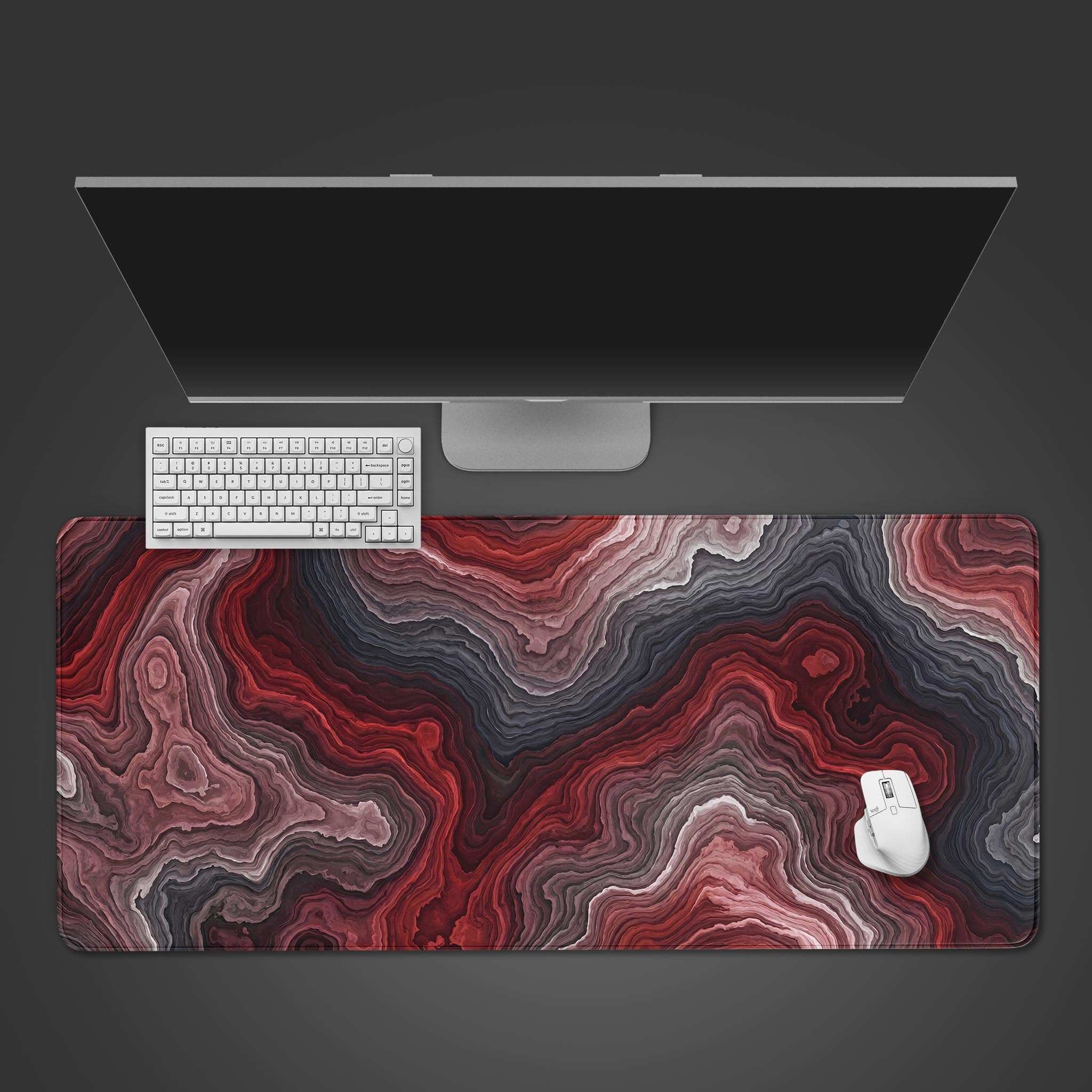 A top-down view of the Crimson Strata gaming desk mat, showcasing its red and black abstract pattern beneath a white keyboard and mouse on a dark surface. - Epic Design Pads & Mousepads