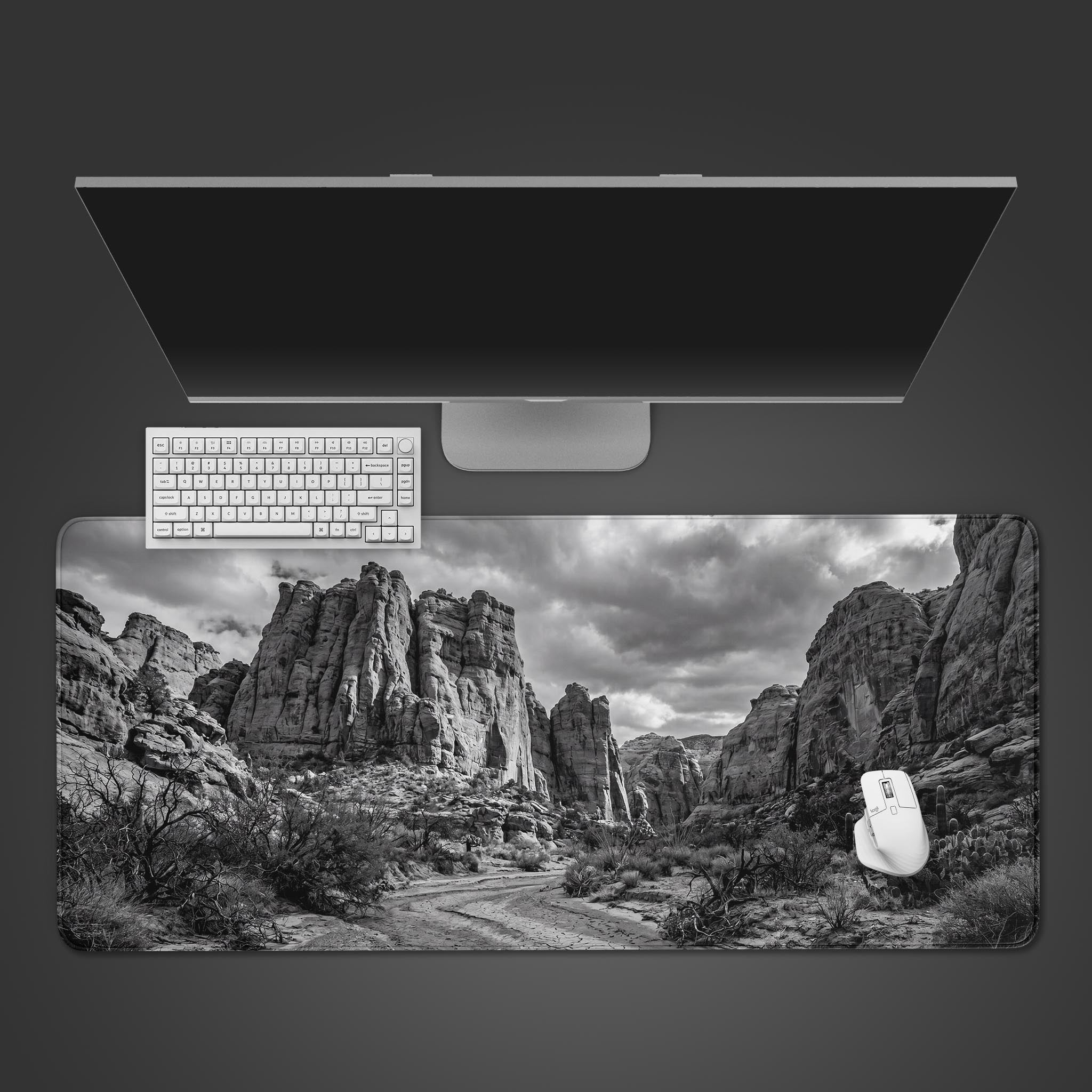 A black and white desk mat featuring a dramatic desert canyon landscape with rocky spires and a dirt trail