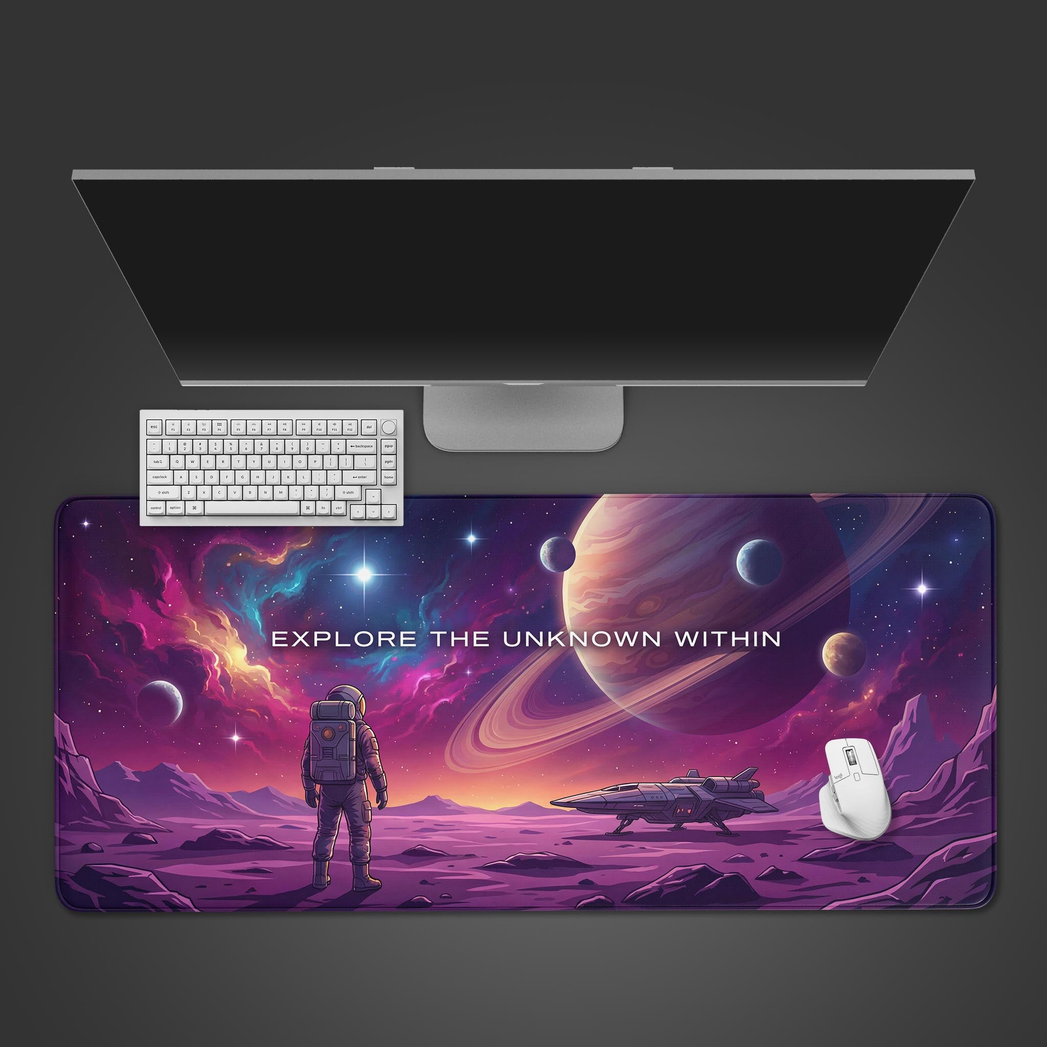 The "Explore The Unknown Within" gaming desk mat shown from above, with a white keyboard and mouse on its cosmic astronaut design, beneath a large monitor. - Epic Design Pads & Mousepads