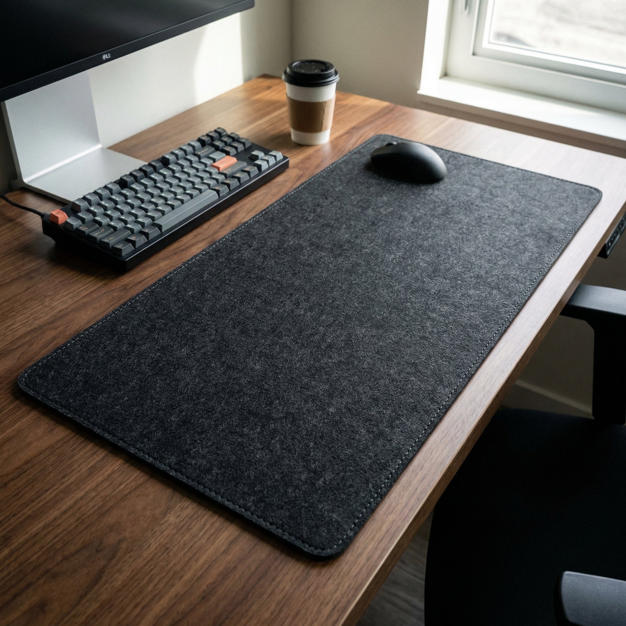 Desk setup with a large black felt mouse pad, keyboard, mouse, and coffee cup.
