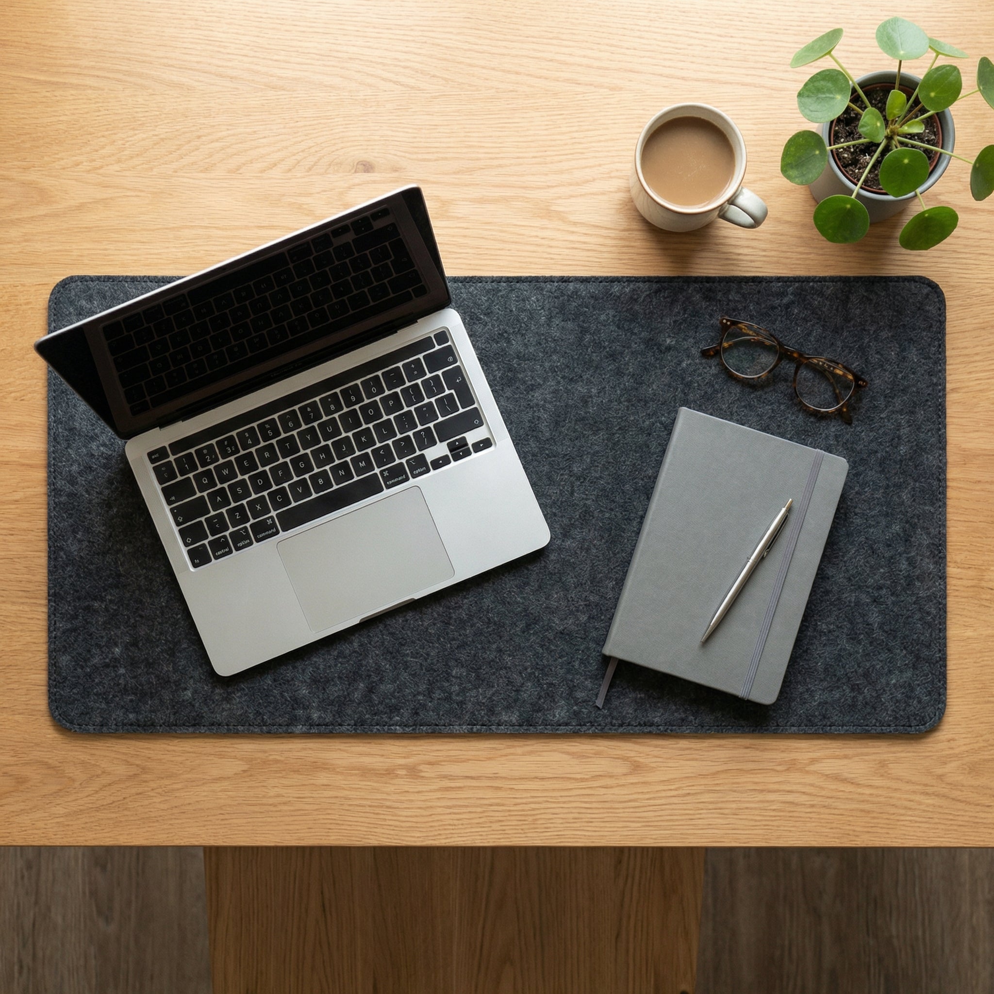 Laptop on a felt desk mat with a notebook, pen, and coffee cup