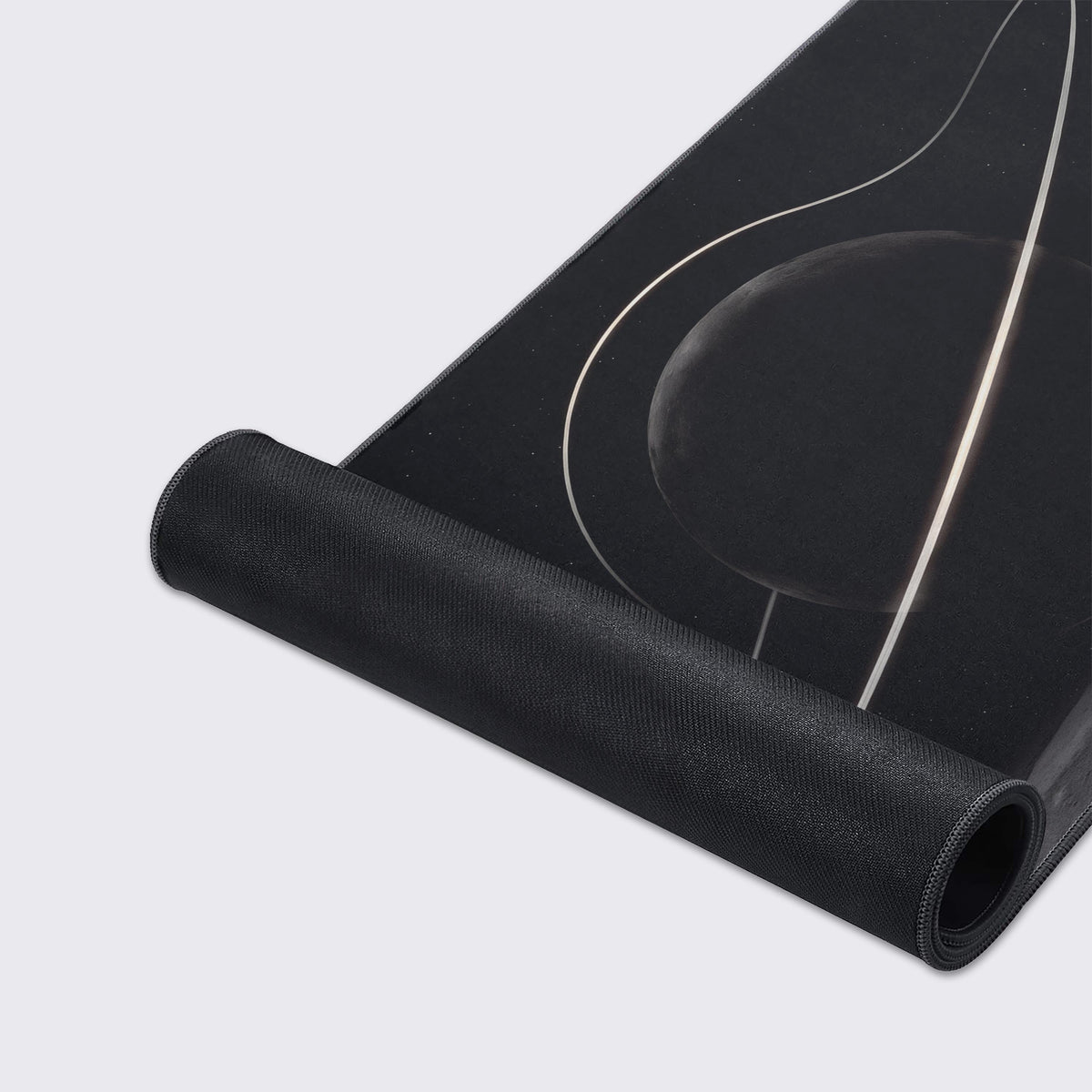 Desk mat partly rolled up, showing its black non-slip rubber underside below the glowing ring and dark moon art