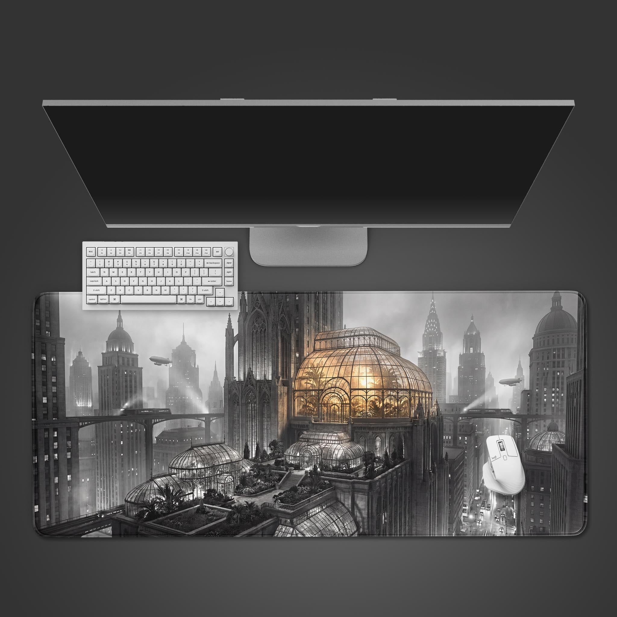 Top-down view of the Industrial Eden gaming desk mat, displaying its monochrome Art Deco city design beneath a white keyboard, mouse, and a large monitor. - Epic Design Pads & Mousepads