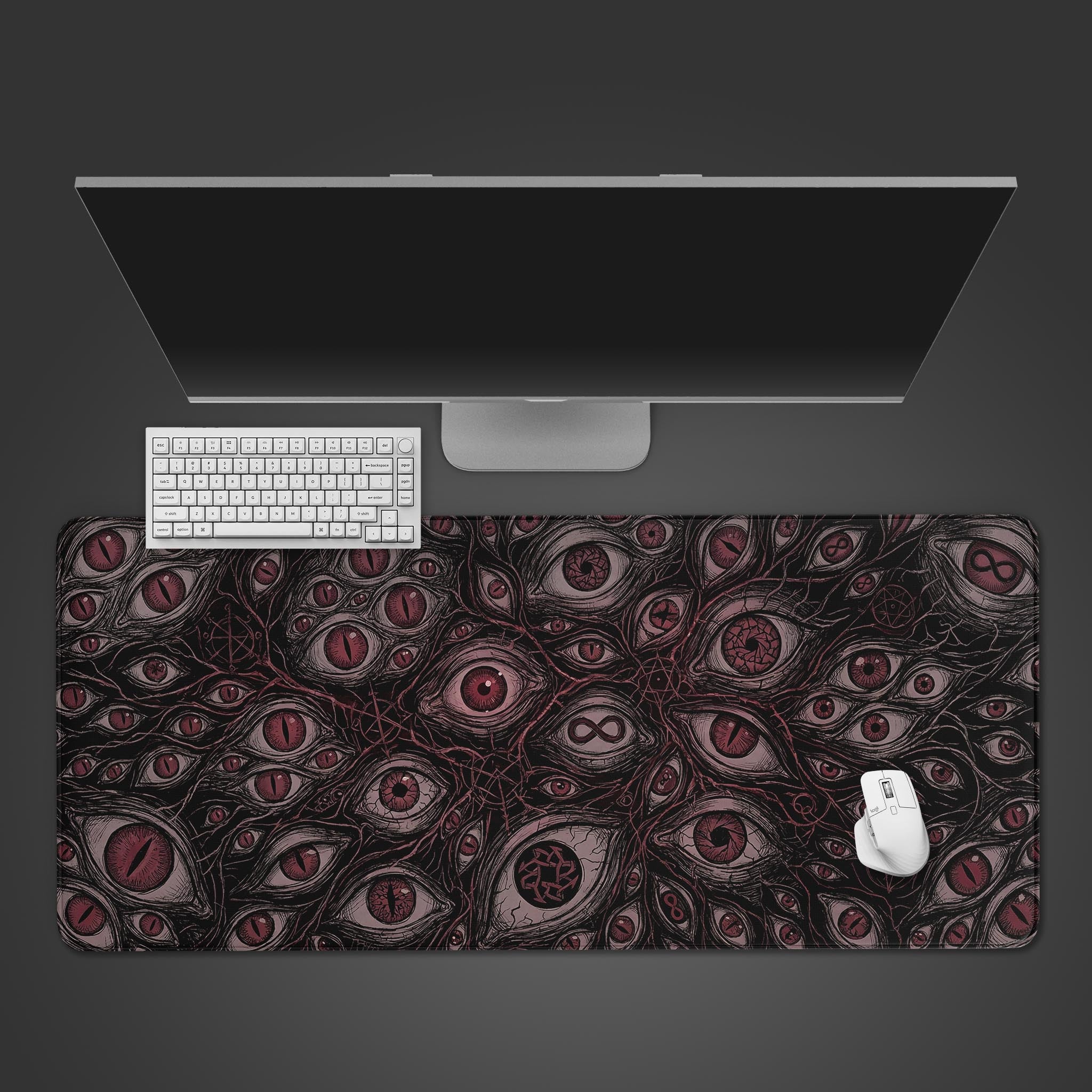 A top-down view of the Omniscient Abyss gaming desk mat, featuring a horror pattern of red eyes, arranged with a white keyboard and mouse under a monitor. - Epic Design Pads & Mousepads