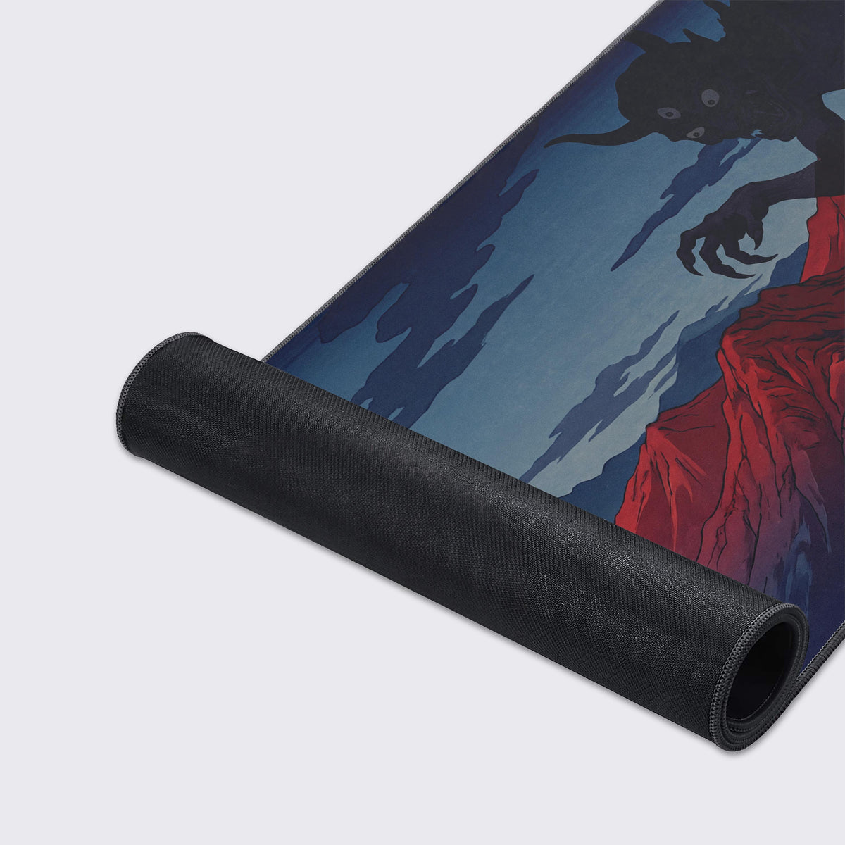 Desk mat partly rolled up to show its black rubber underside, beside art of a horned demon's claws over a red cliff