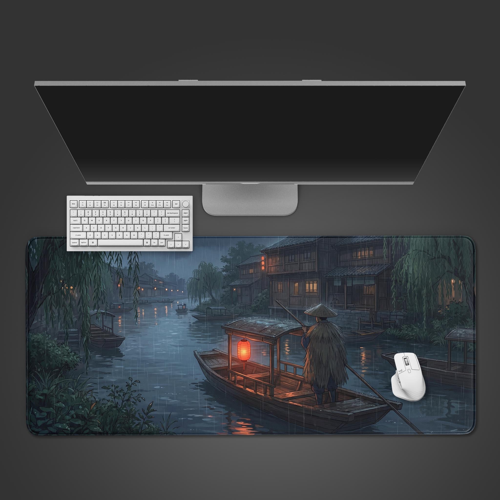 Top-down view of the Silent Boatman gaming desk mat, showing the rainy river town design beneath a white keyboard, mouse, and monitor on a dark surface. - Epic Design Pads & Mousepads