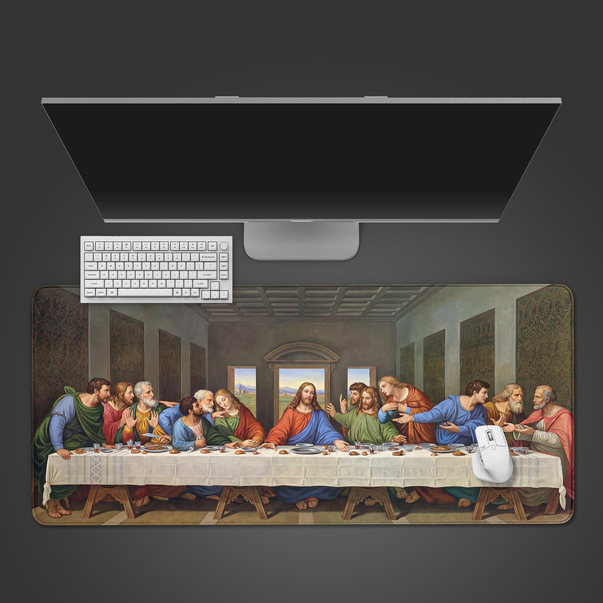 A top-down view of a desk setup featuring The Last Supper gaming desk mat by Leonardo da Vinci, with a white keyboard and monitor on a dark gray surface. - Epic Design Pads & Mousepads