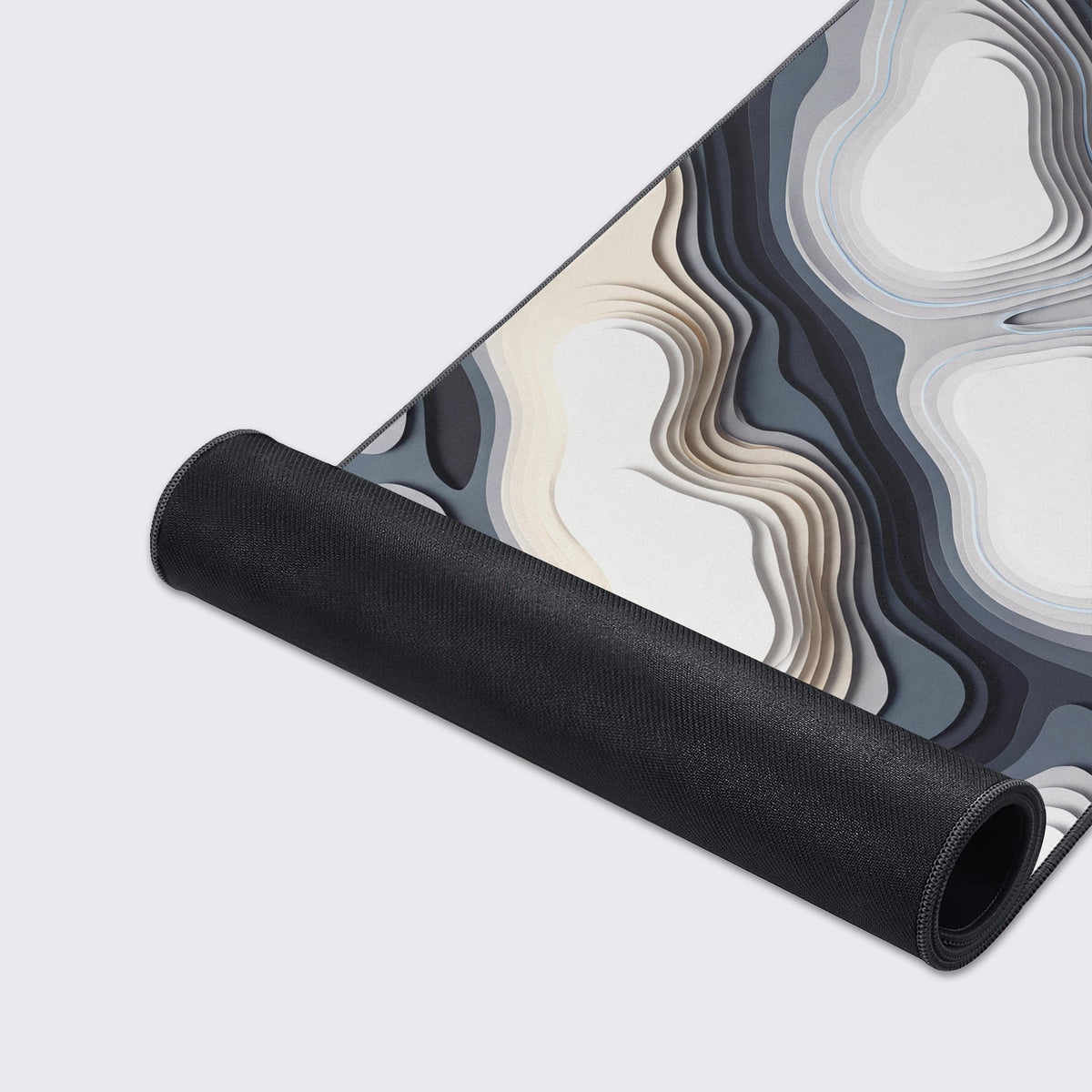 Desk mat rolled up to show its black non-slip rubber underside below the white, beige and gray layered contour art