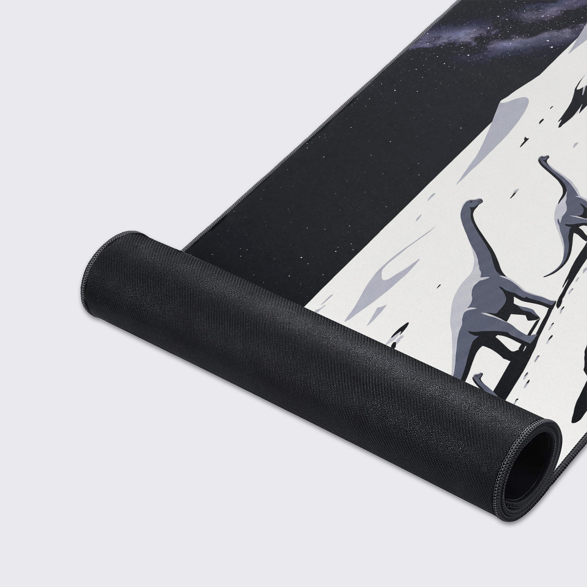 Rolled-up desk mat showing its black rubber underside beside printed grey sauropods on a moonscape under stars