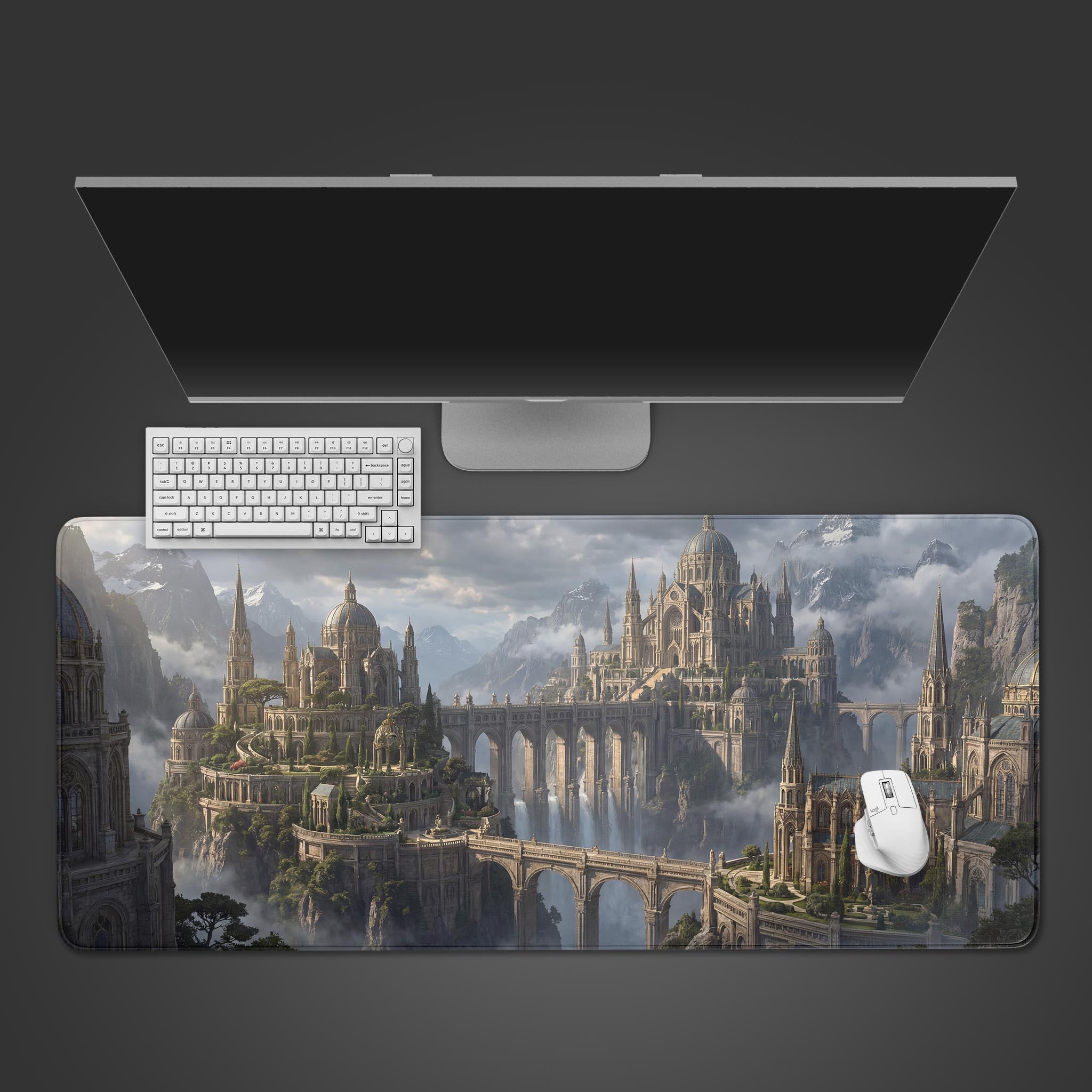 A top-down view of the Aethelgard Ascent gaming desk mat, showcasing a fantasy mountain city. A white keyboard and mouse are positioned on the mat below a monitor. - Epic Design Pads & Mousepads