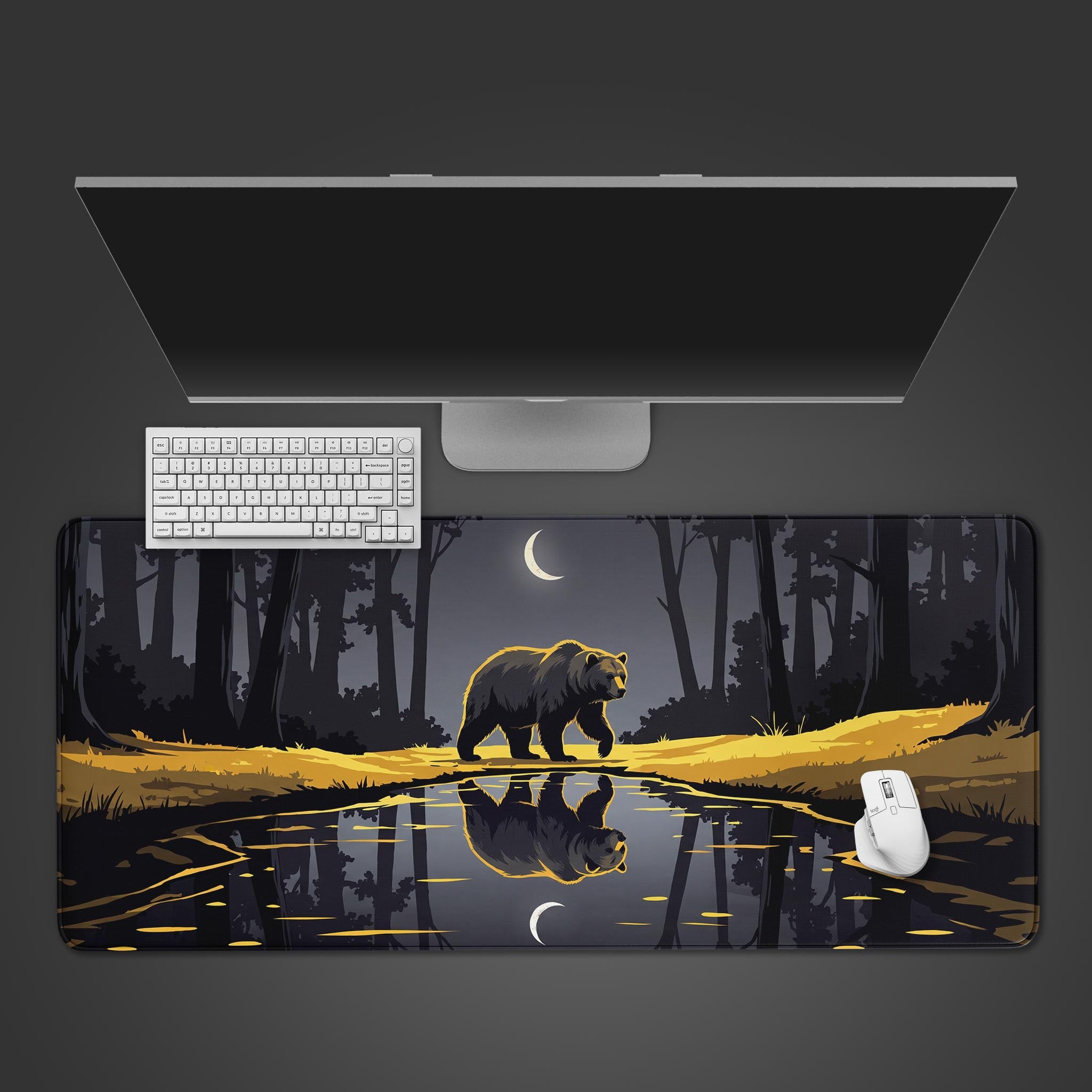 A wide desk mat displaying a bear walking by a reflective river at night, illuminated by a crescent moon