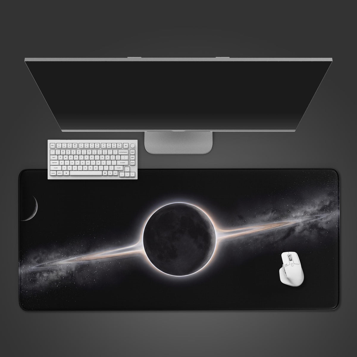 A sleek black desk mat featuring a dark unlit moon surrounded by a glowing cosmic ring against a starry space background