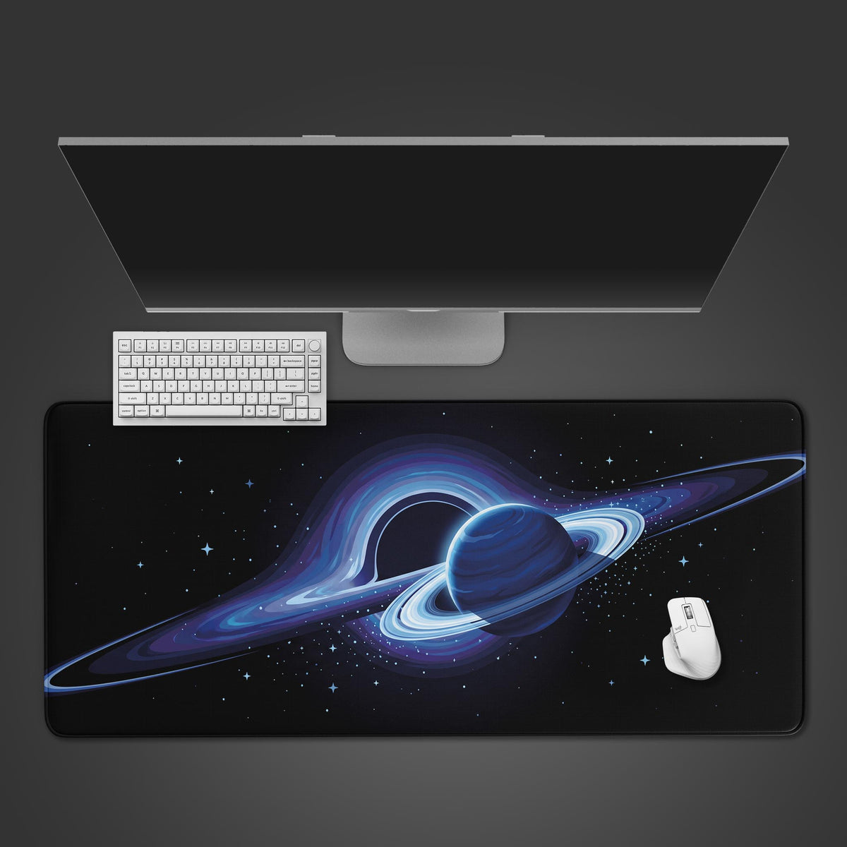 Blue crescent black hole space desk mat from above with a ringed planet, white keyboard, white mouse and silver monitor.