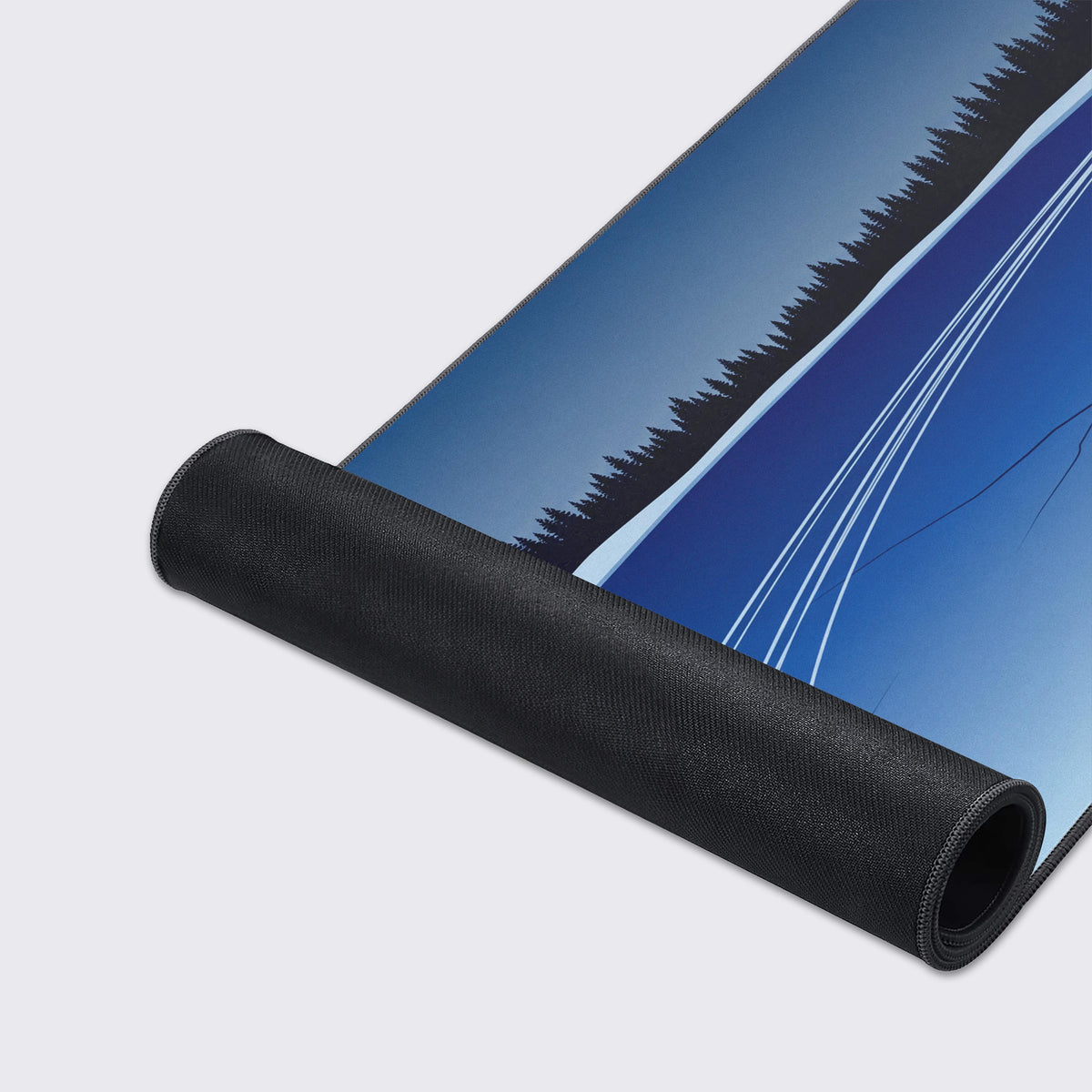 Partly rolled desk mat showing its black rubber underside below blue frozen lake art with pine trees and white skate lines