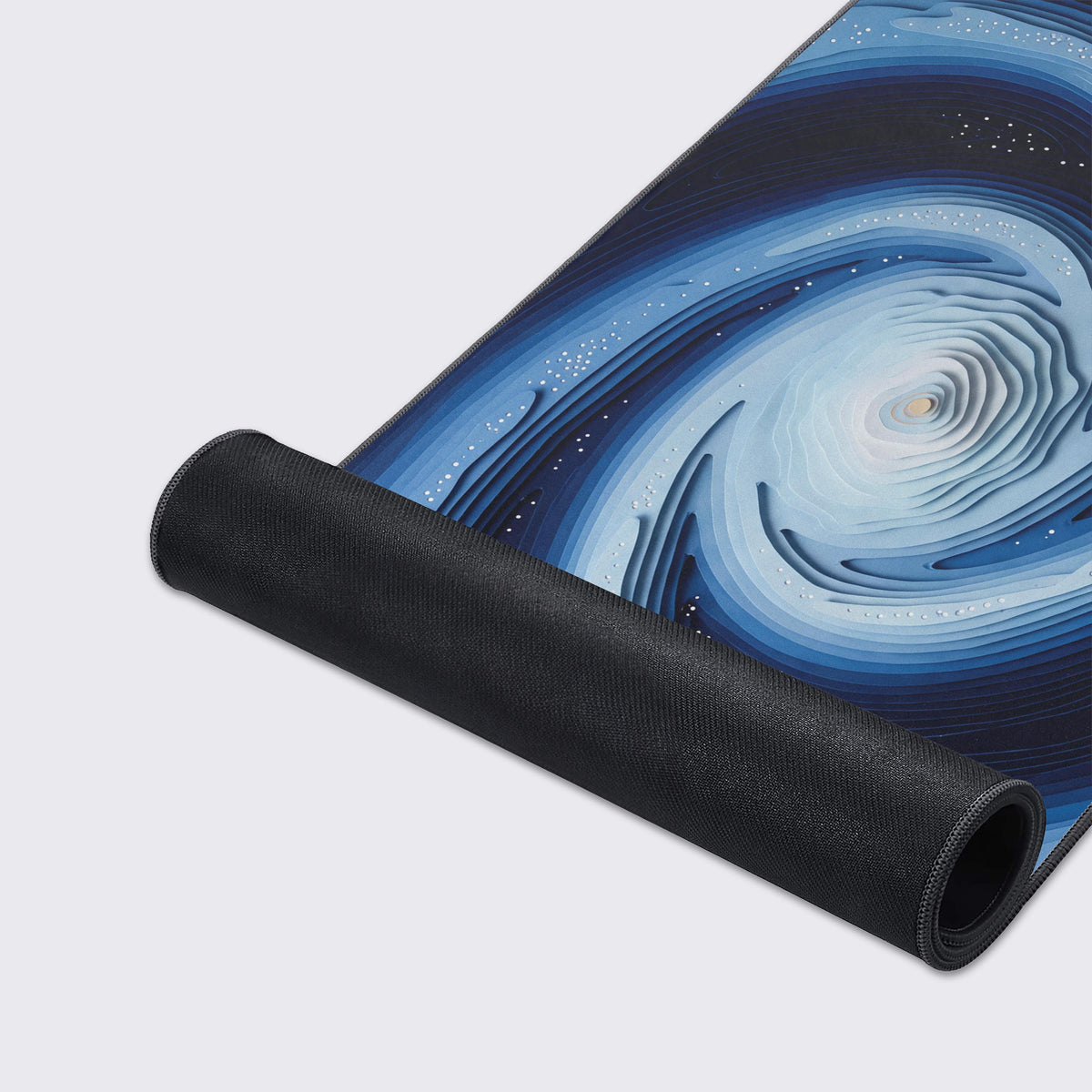Desk mat partly rolled up on a light grey surface, showing its black rubber underside and layered blue spiral galaxy art