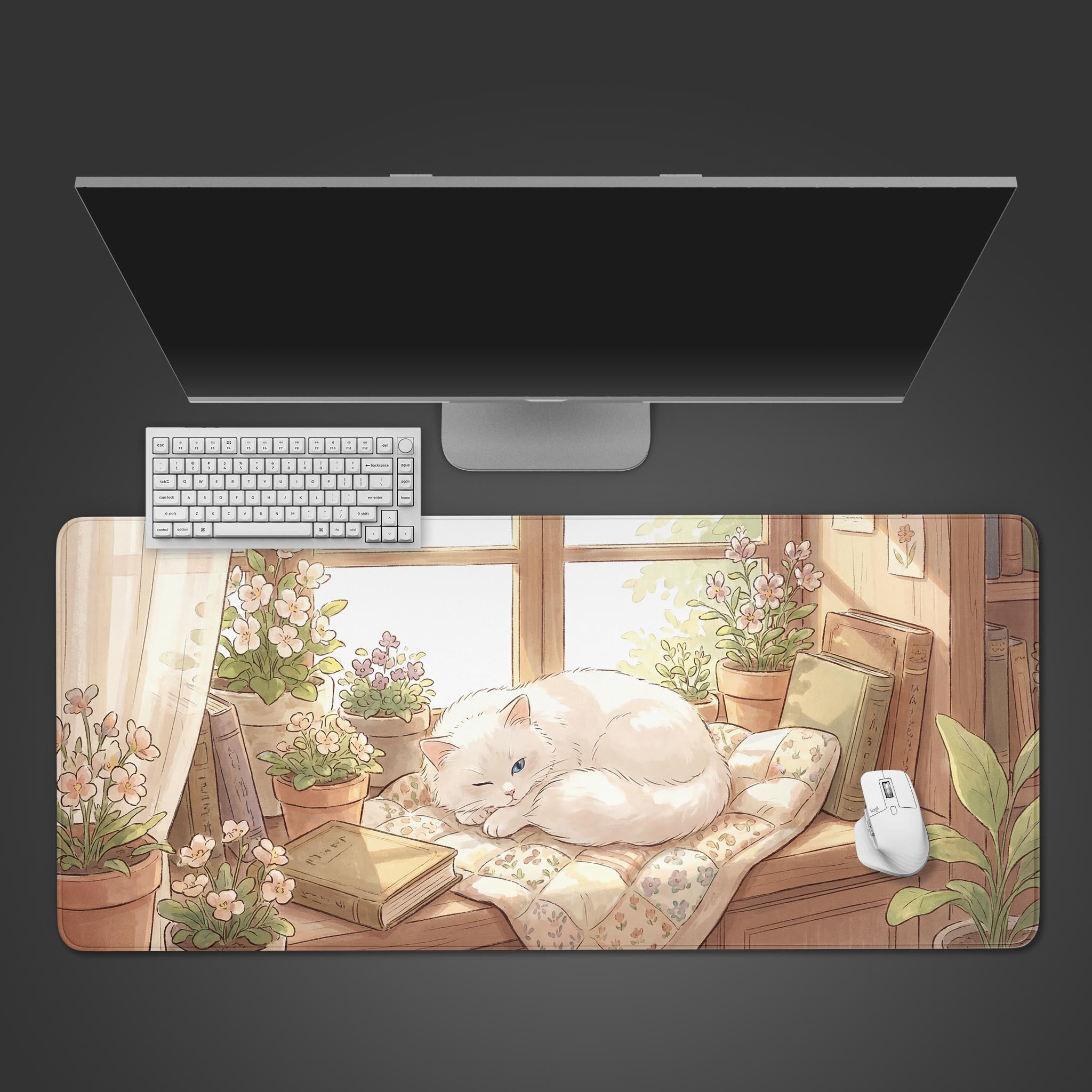 Top-down view of the Bookish Nap gaming desk mat, showing the cozy cat and book design alongside a white keyboard, mouse, and sleek monitor on a dark background. - Epic Design Pads & Mousepads