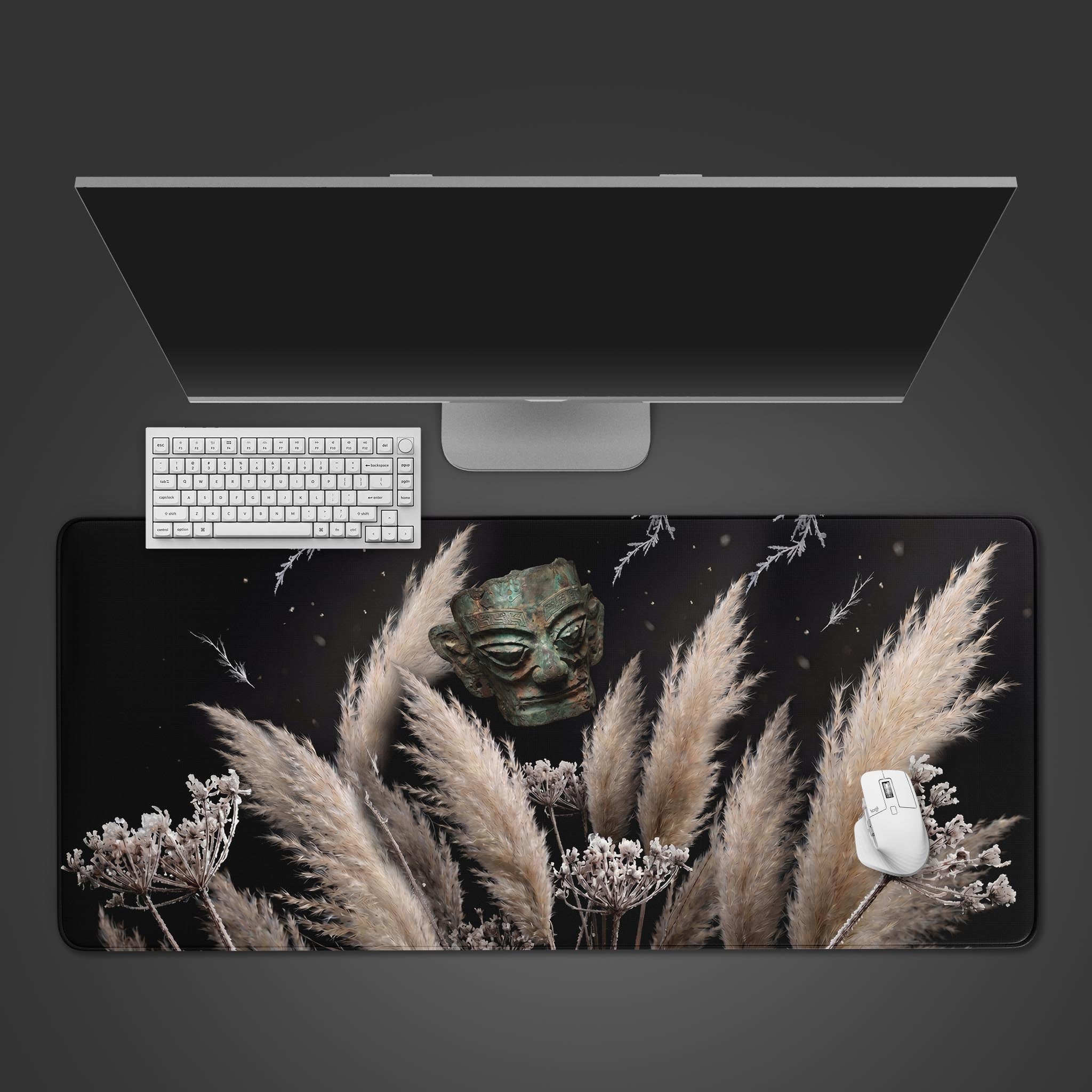 Ancient bronze mask hovering over frosted pampas grass on an XL desk mat