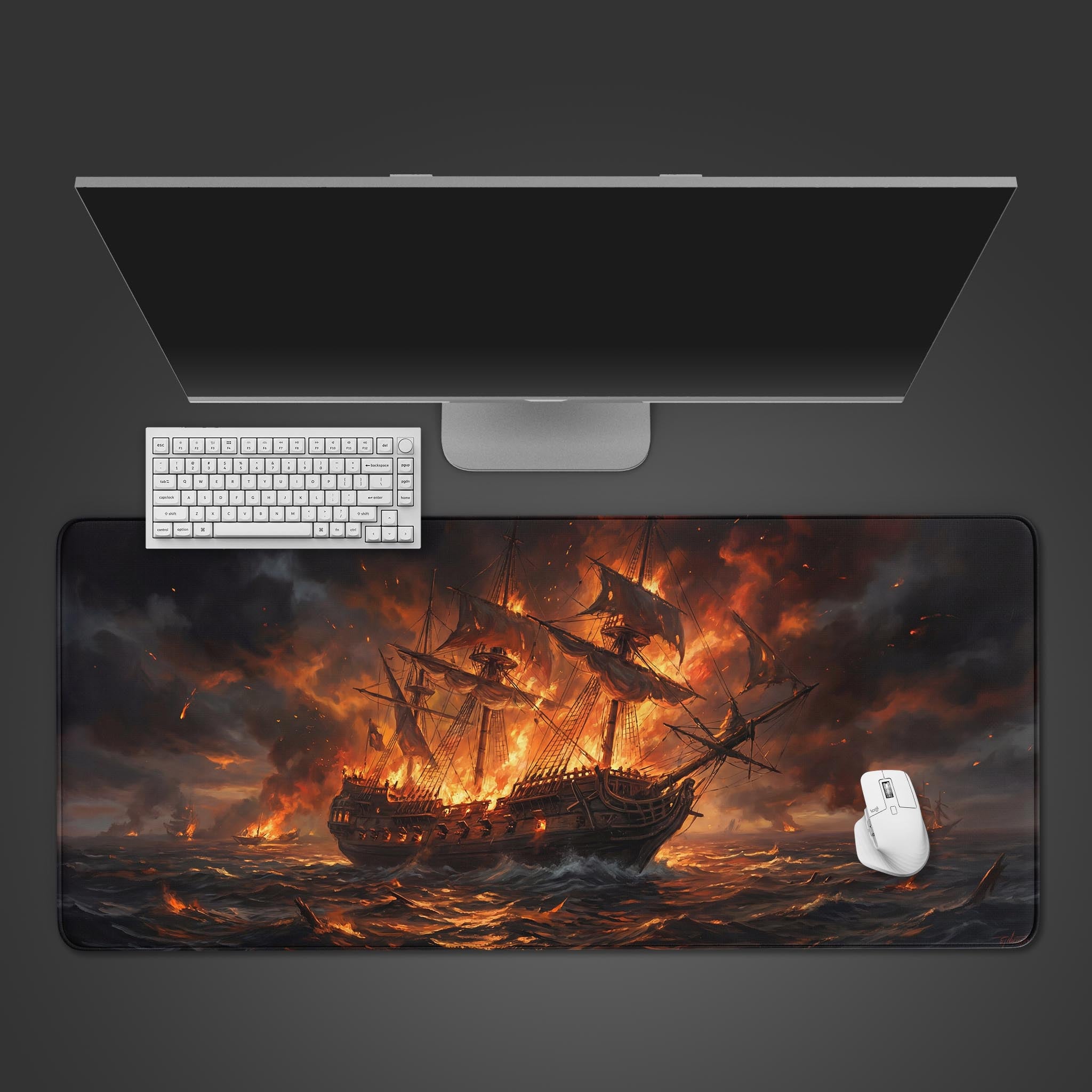 A top-down view of the Burning Galleon gaming desk mat on a desk, with a white keyboard and mouse placed on it under a large monitor. - Epic Design Pads & Mousepads