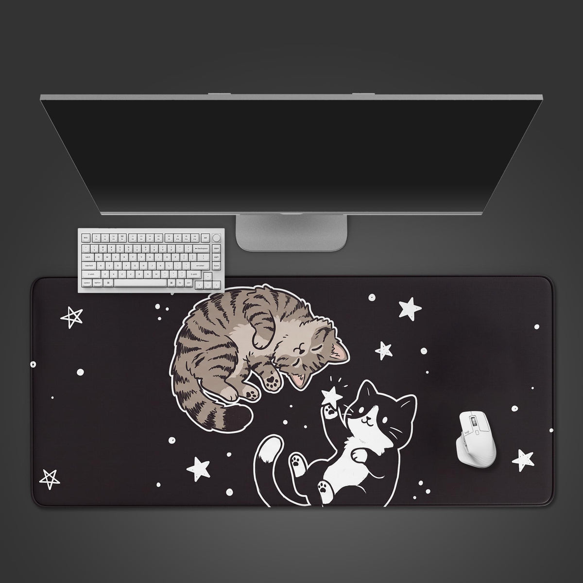 Desk mat featuring a cute brown tabby sleeping and a black tuxedo cat playing with stars on a black background.