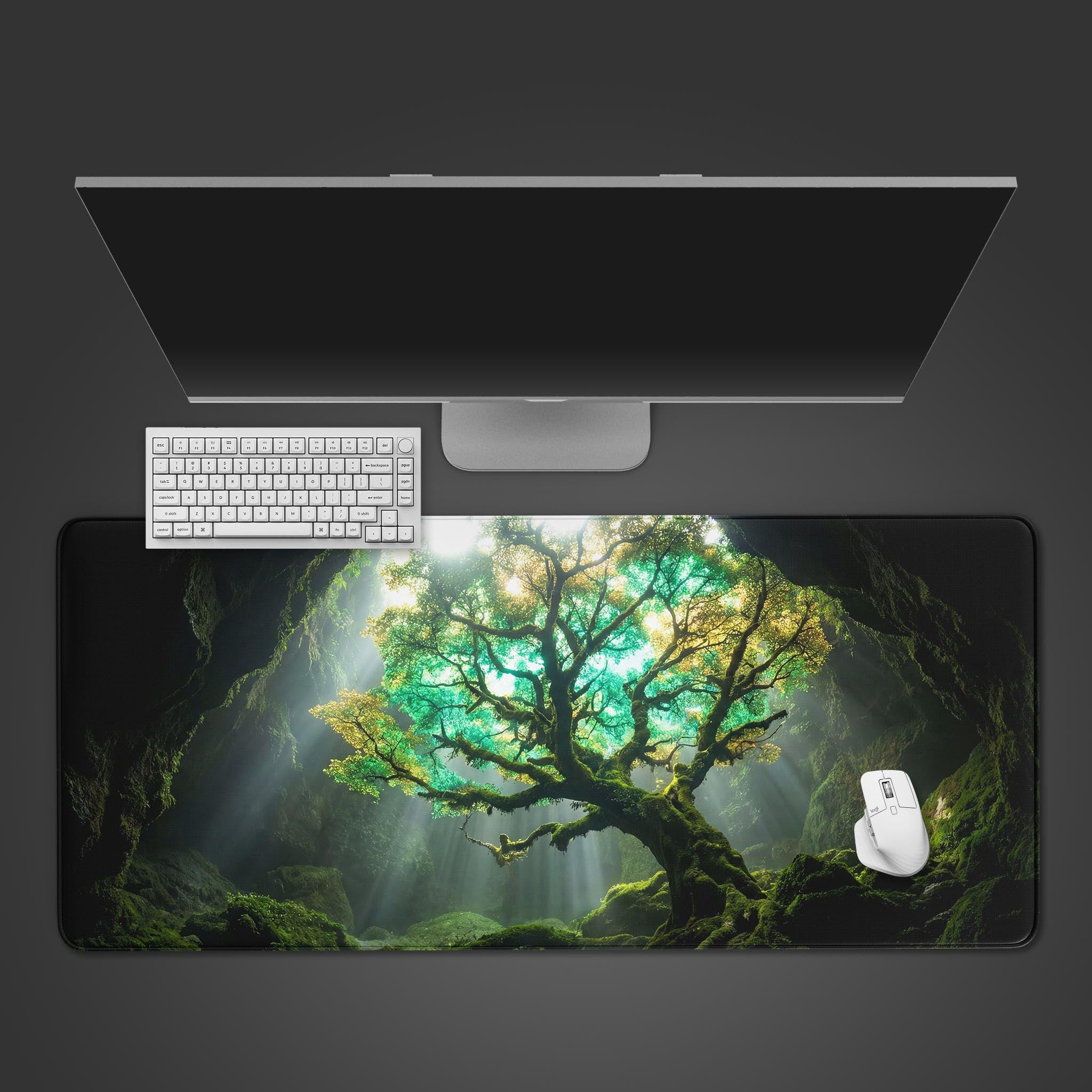 A top-down view of the Cavern Light gaming desk mat, showing the enchanted tree design beneath a white keyboard, mouse, and computer monitor on a dark background. - Epic Design Pads & Mousepads