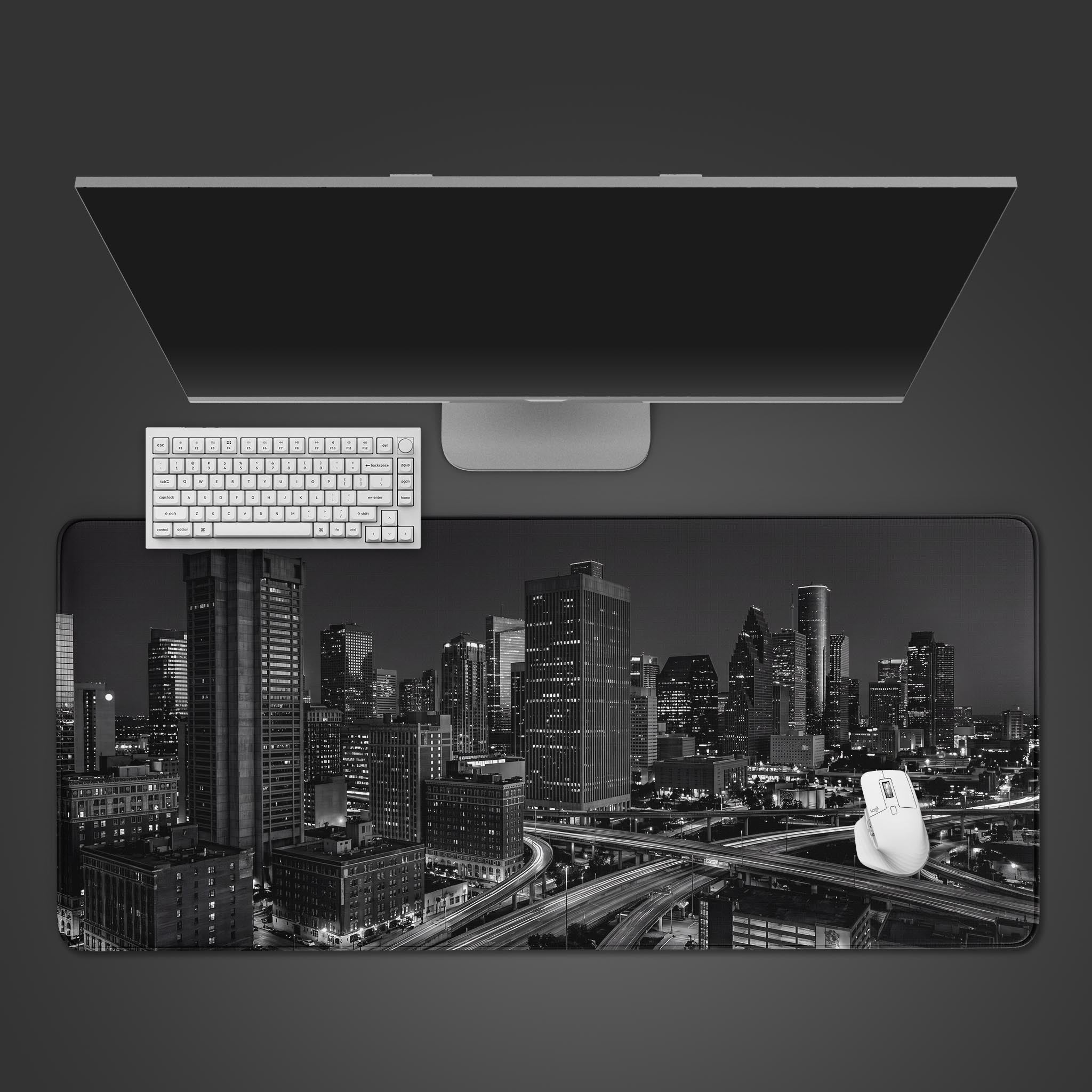 A wide desk mat displaying a high-contrast black and white photograph of a city skyline at night with a complex highway system.