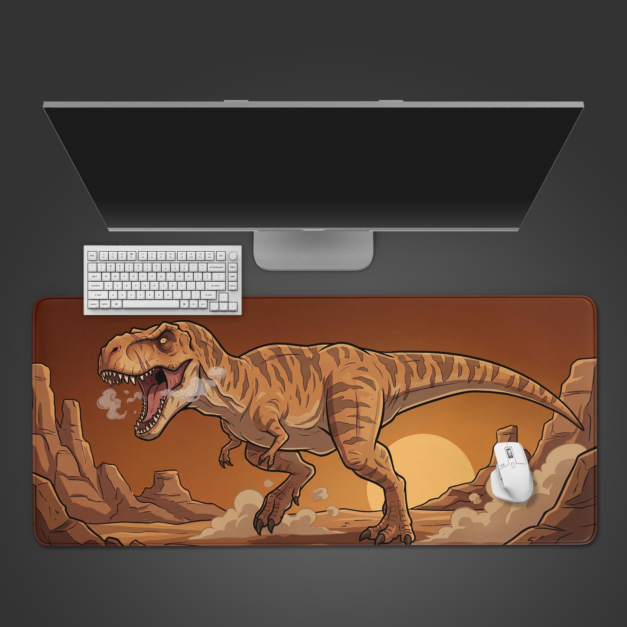 A top-down view of the Desert Tyrant gaming desk mat, featuring a roaring T-Rex. A white keyboard and mouse are placed on it, below a large monitor. - Epic Design Pads & Mousepads