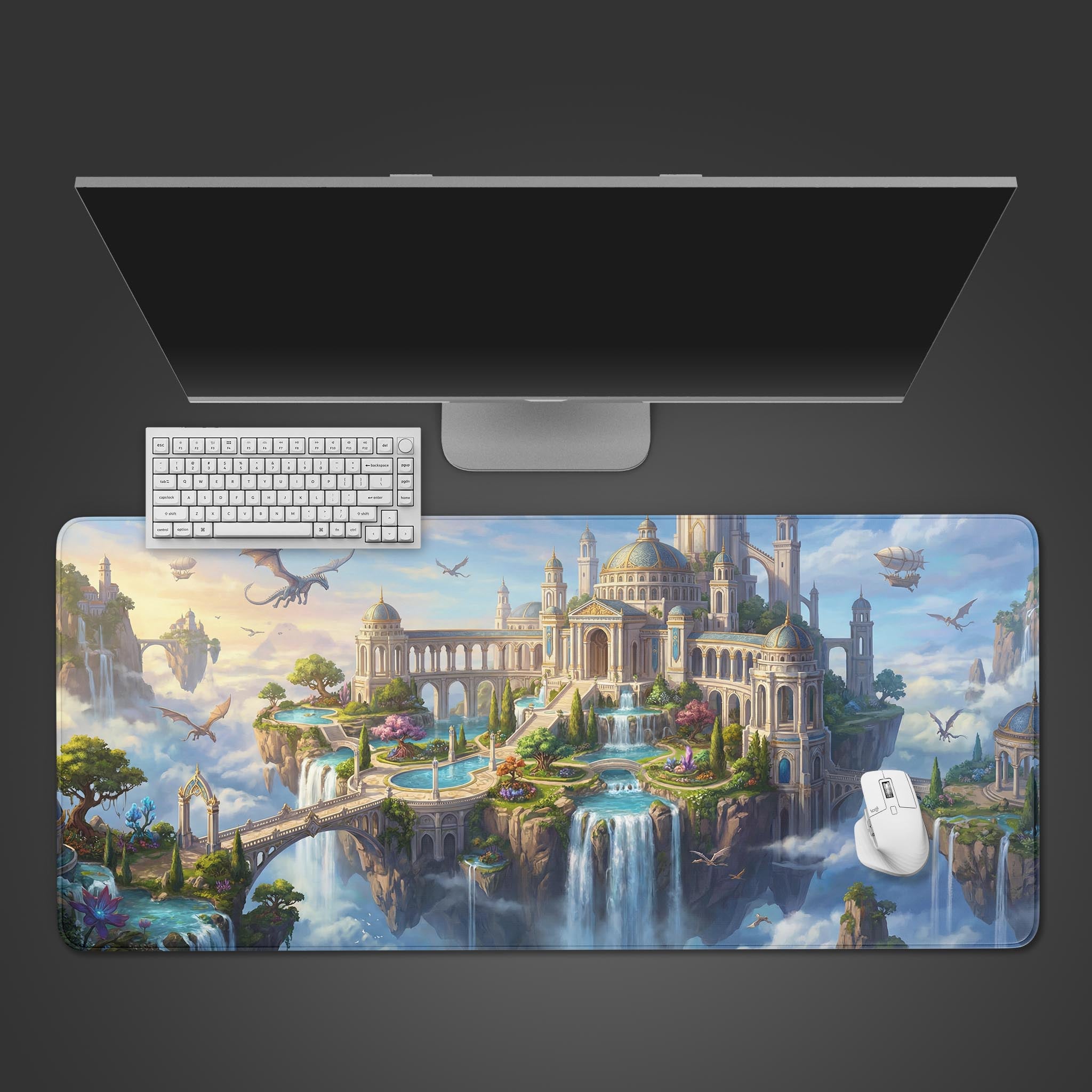 A top-down view of the Dragon's Aether Peak gaming desk mat with its floating castle art. A white keyboard and mouse are placed on top, beneath a large monitor. - Epic Design Pads & Mousepads
