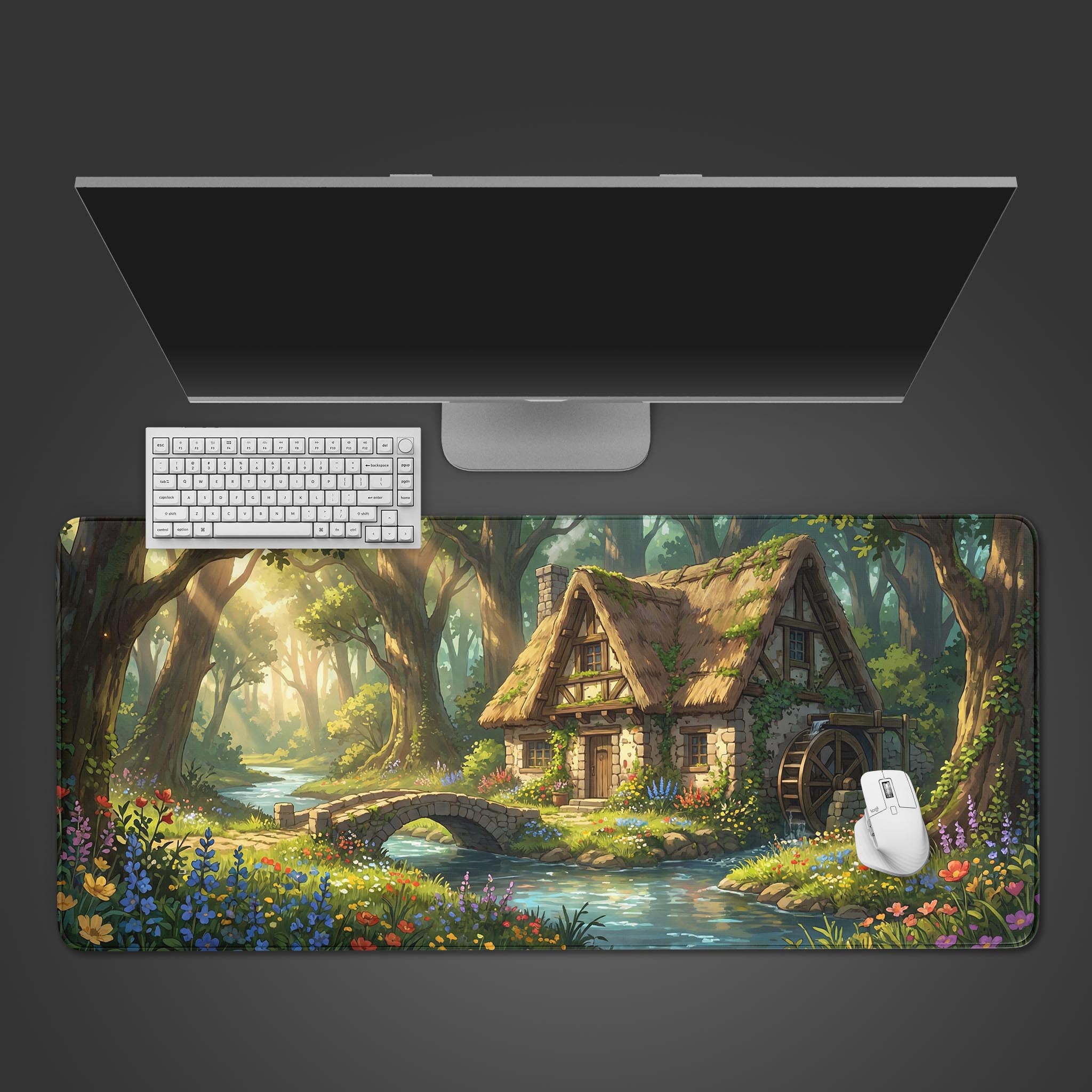 Top-down view of the Enchanted Mill gaming desk mat, showcasing its serene forest cottage design alongside a white keyboard, mouse, and a large monitor on a dark surface. - Epic Design Pads & Mousepads