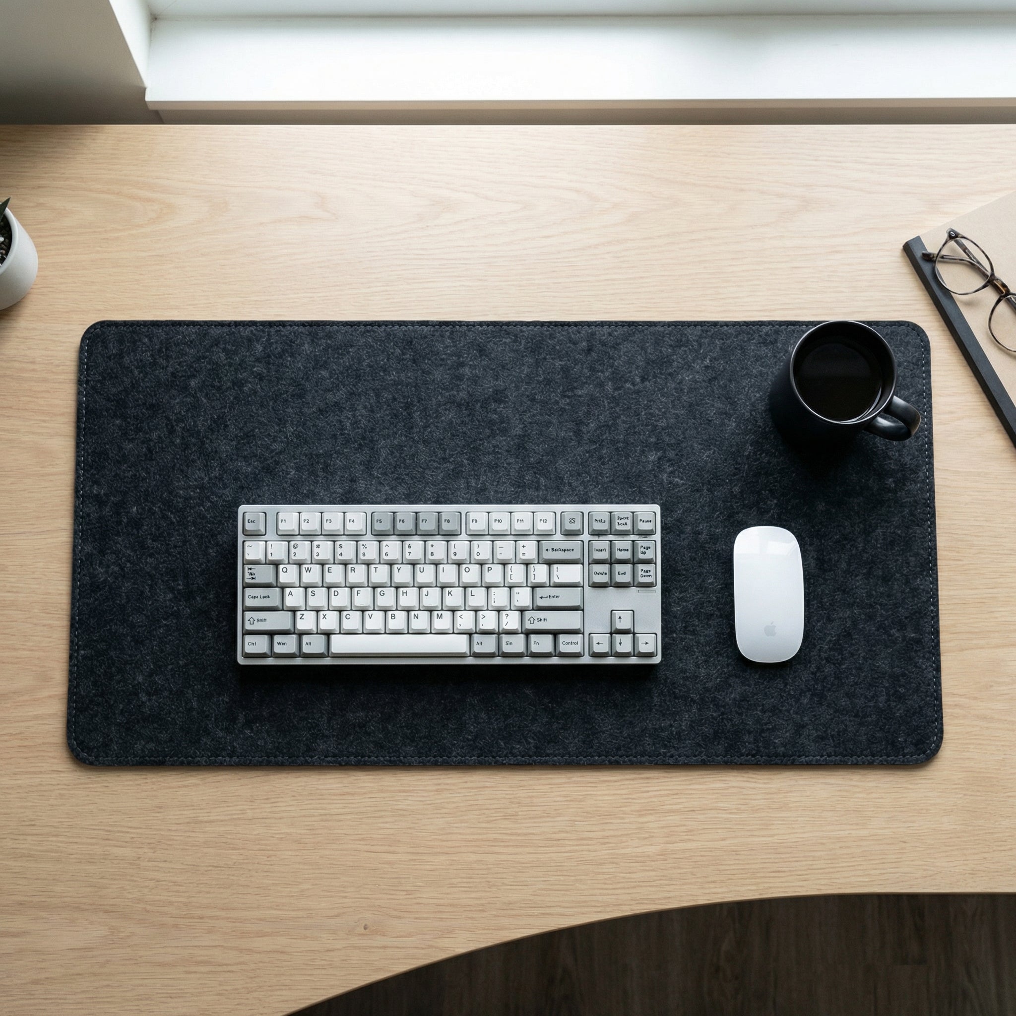 Desk setup with keyboard, mouse, and mug on a large black felt mouse pad.