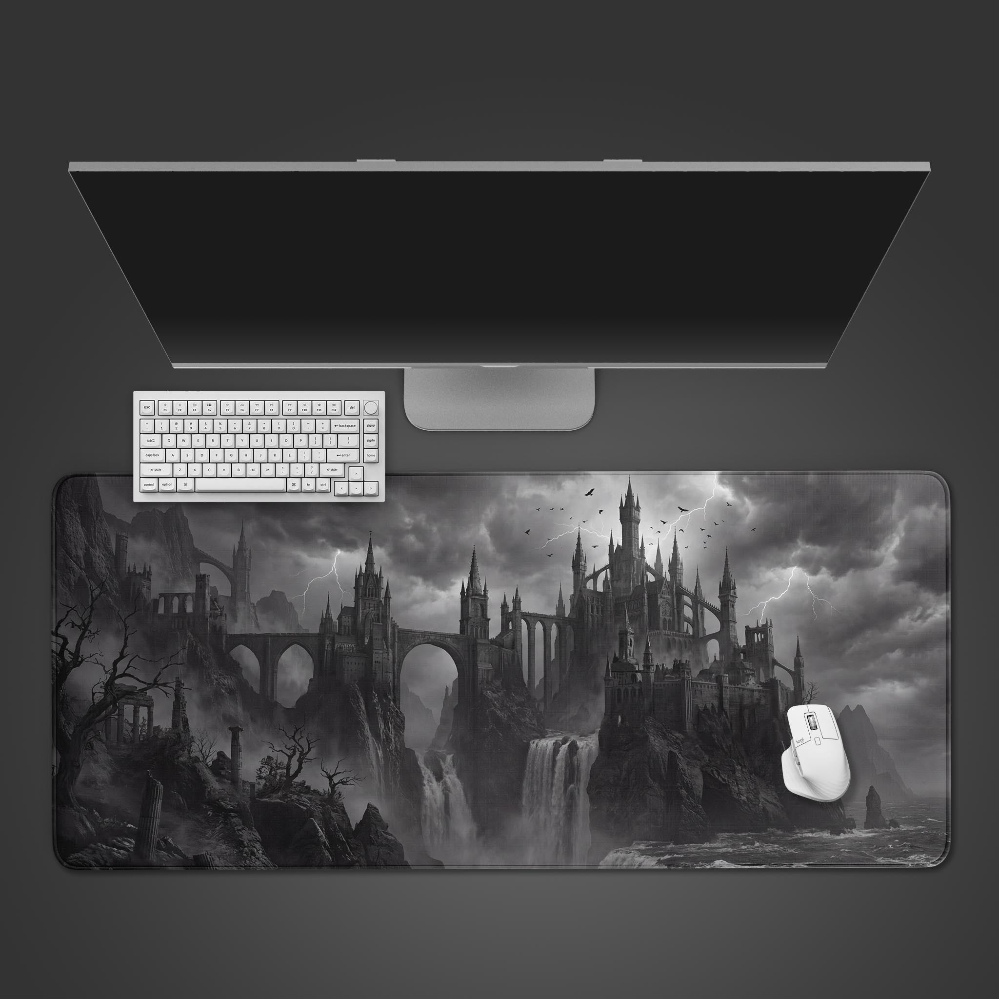 A top-down view of the Forgotten Fortress gaming desk mat, showing the monochrome gothic castle design alongside a white keyboard, mouse, and a large monitor on a dark surface. - Epic Design Pads & Mousepads