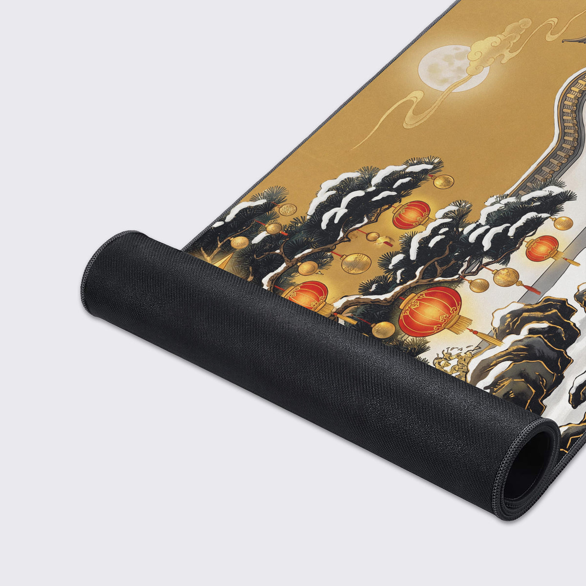 Desk mat rolled up on grey showing black rubber underside and art of snowy pines, red lanterns and a full moon