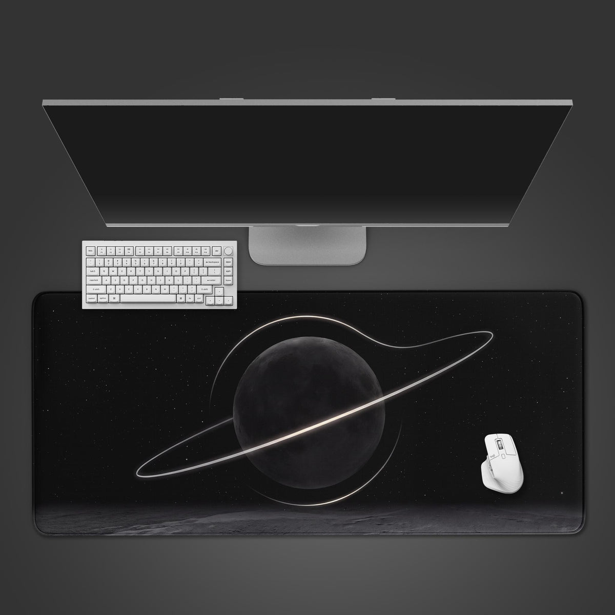 Gray half moon black hole space desk mat from above, with a monitor, white keyboard and mouse; glowing ring on a dark moon