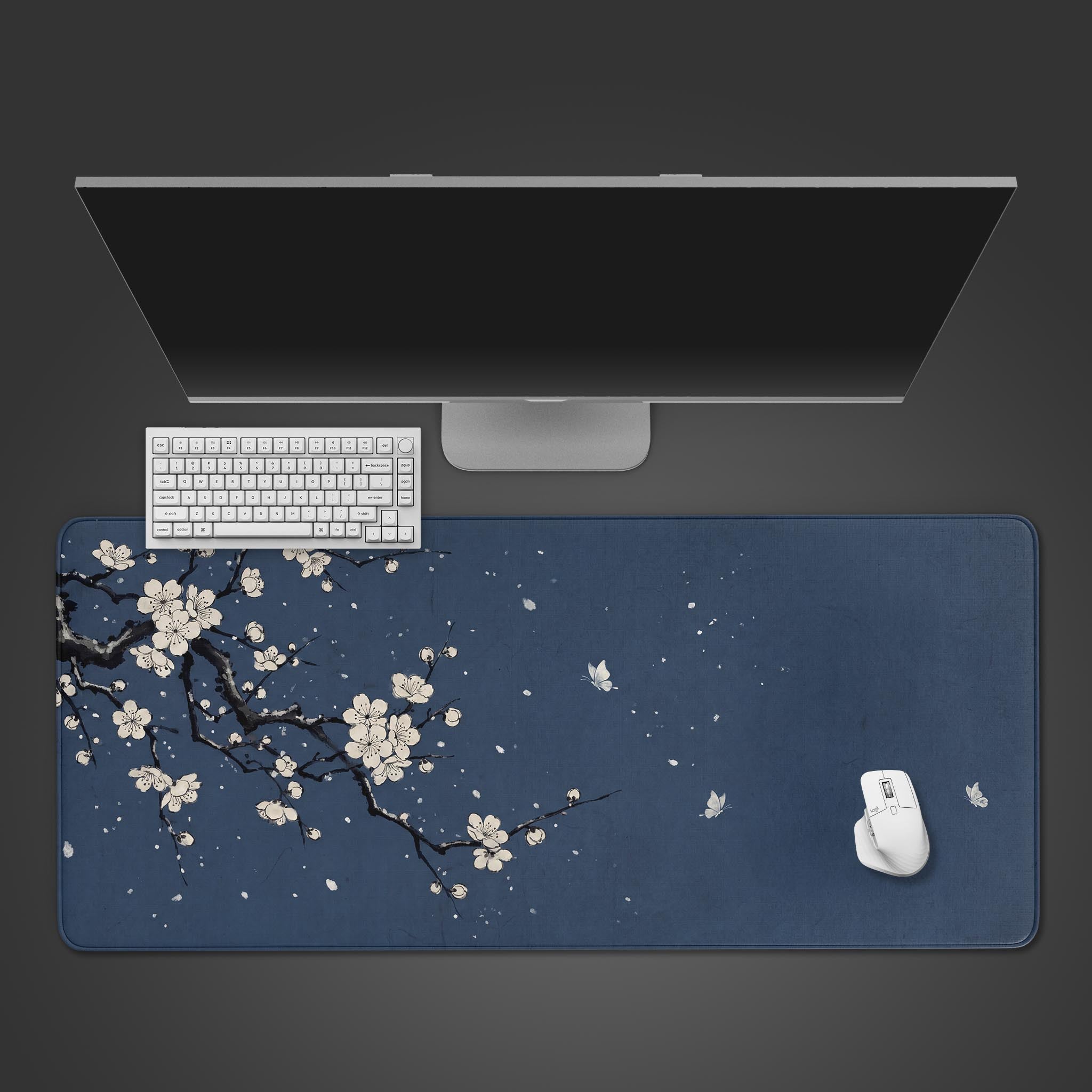 Top-down view of the Indigo Sakura gaming desk mat, featuring a Japanese cherry blossom design, with a white keyboard and mouse neatly arranged on its deep blue surface. - Epic Design Pads & Mousepads