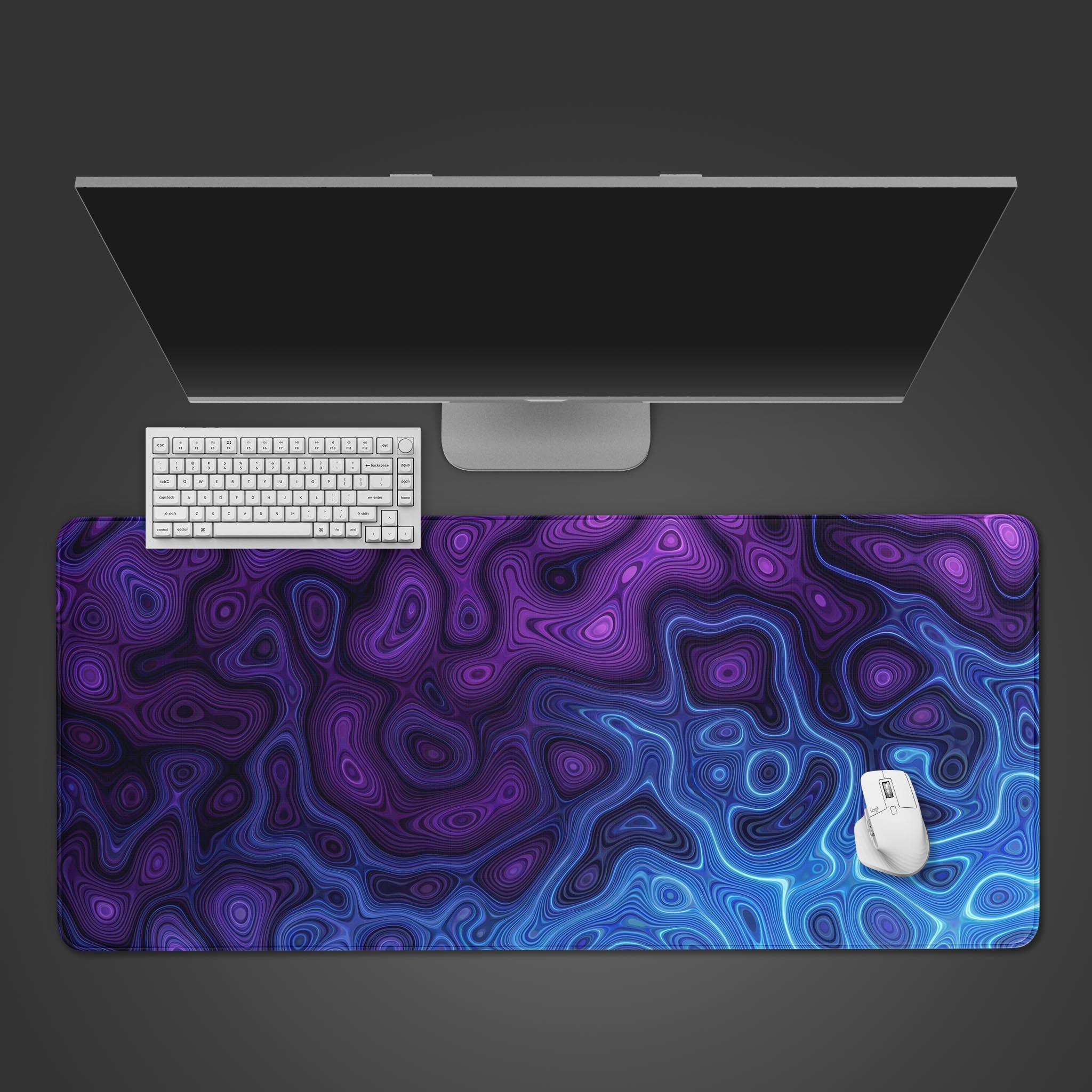 A top-down view of the Neon Damascus gaming desk mat, featuring its abstract purple and blue pattern. A white keyboard and mouse are positioned on the mat below a monitor. - Epic Design Pads & Mousepads