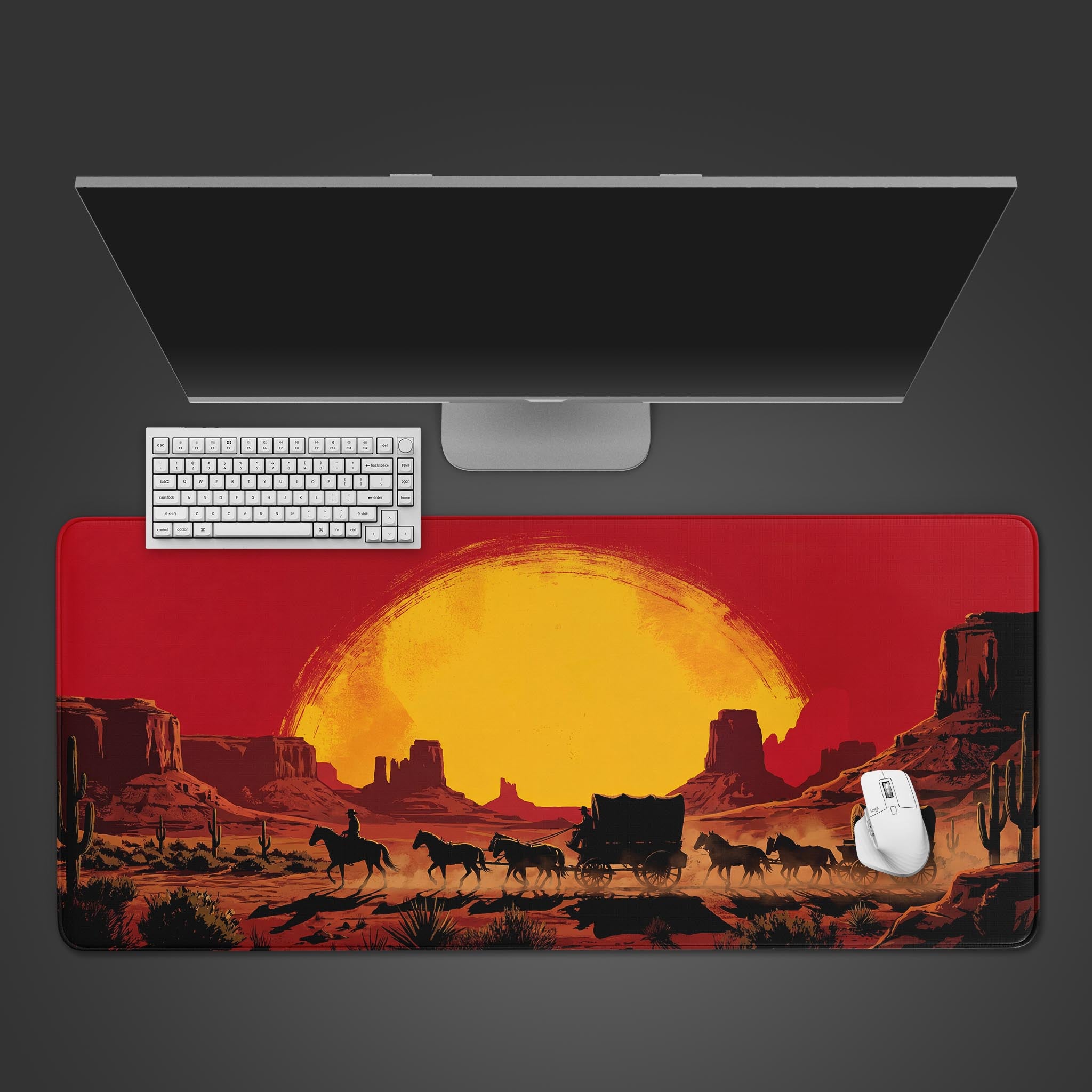 A top-down view of the Outlaw's Path gaming desk mat, showing its red western sunset design beneath a sleek white keyboard, mouse, and a large monitor. - Epic Design Pads & Mousepads