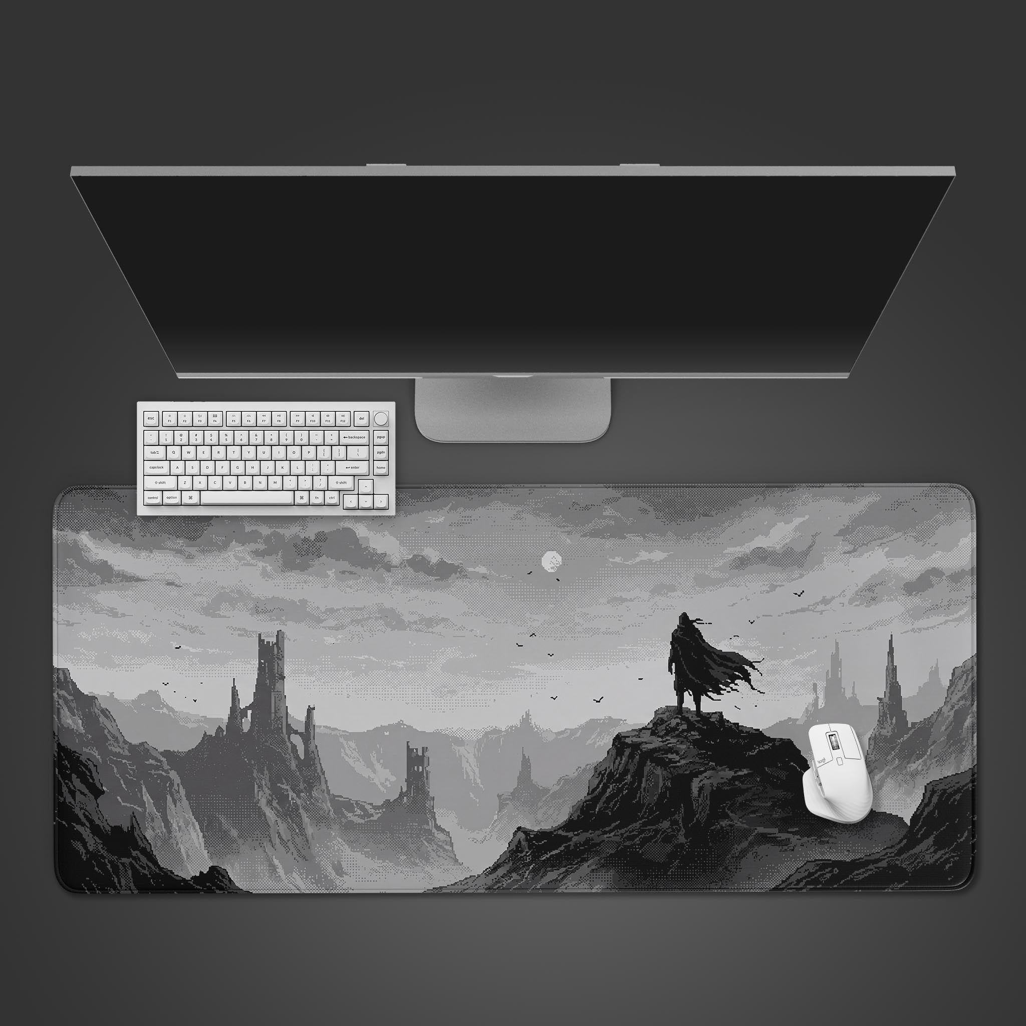 A grayscale pixel art desk mat featuring a cloaked wanderer standing on a mountain peak looking at distant ruined castles.