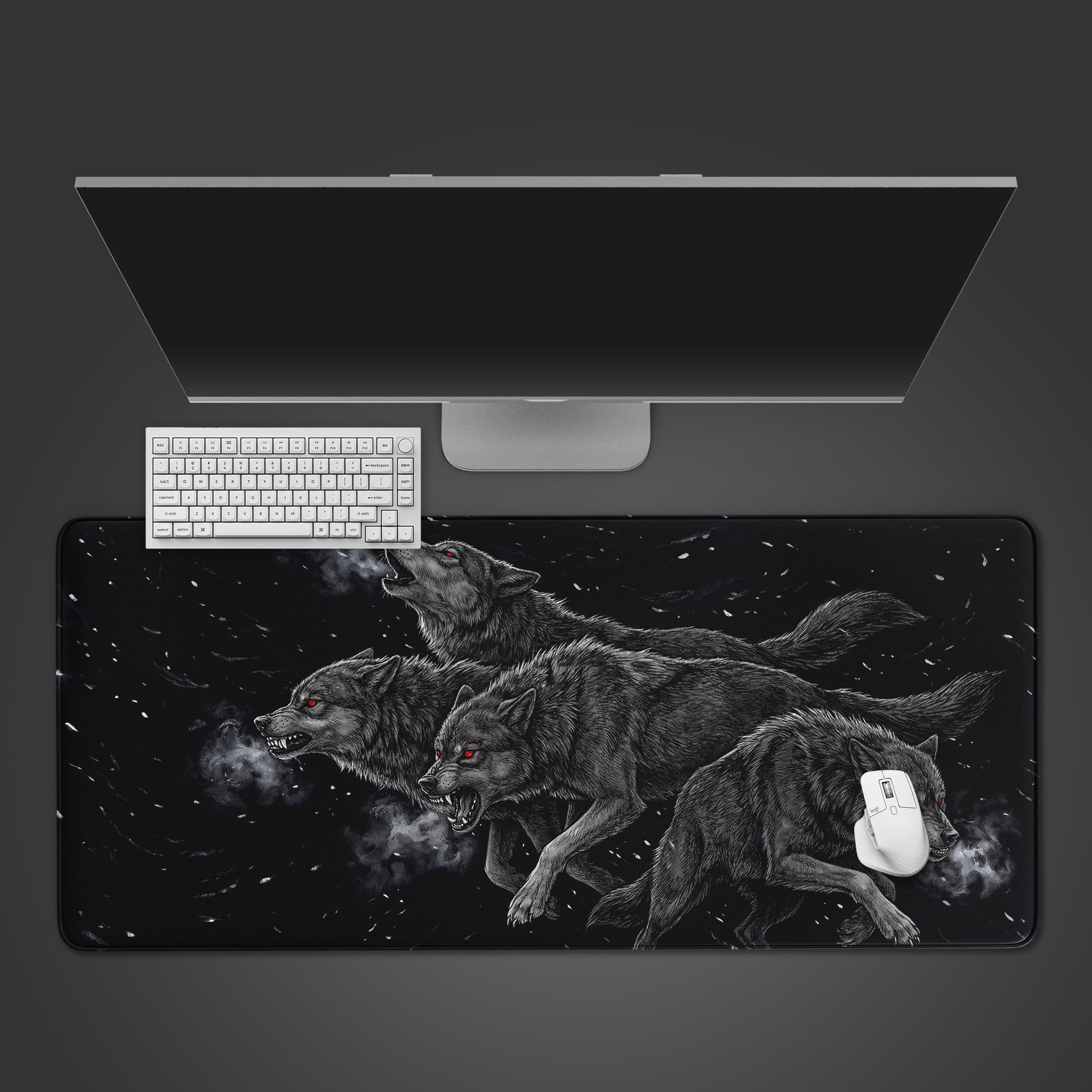 A top-down view of the Relentless Pack gaming desk mat featuring aggressive wolves. A white keyboard and mouse are placed on top, below a large monitor, showing its scale. - Epic Design Pads & Mousepads