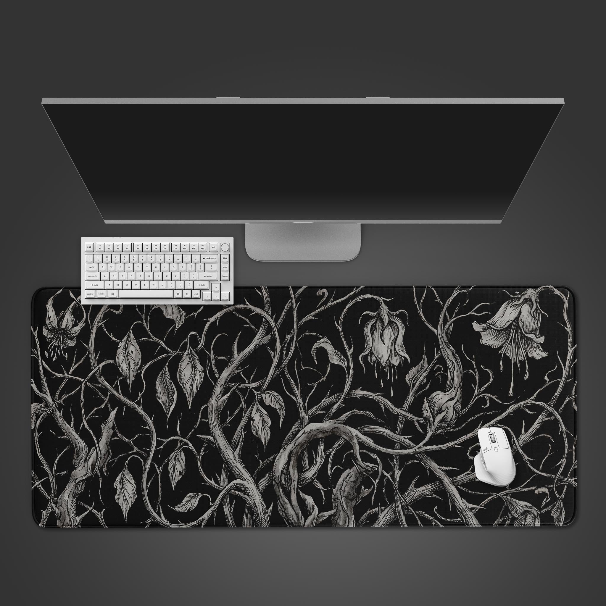 A top-down view of the Shadow Vines gaming desk mat, featuring a dark floral vine pattern, shown with a white keyboard and mouse on a dark background. - Epic Design Pads & Mousepads