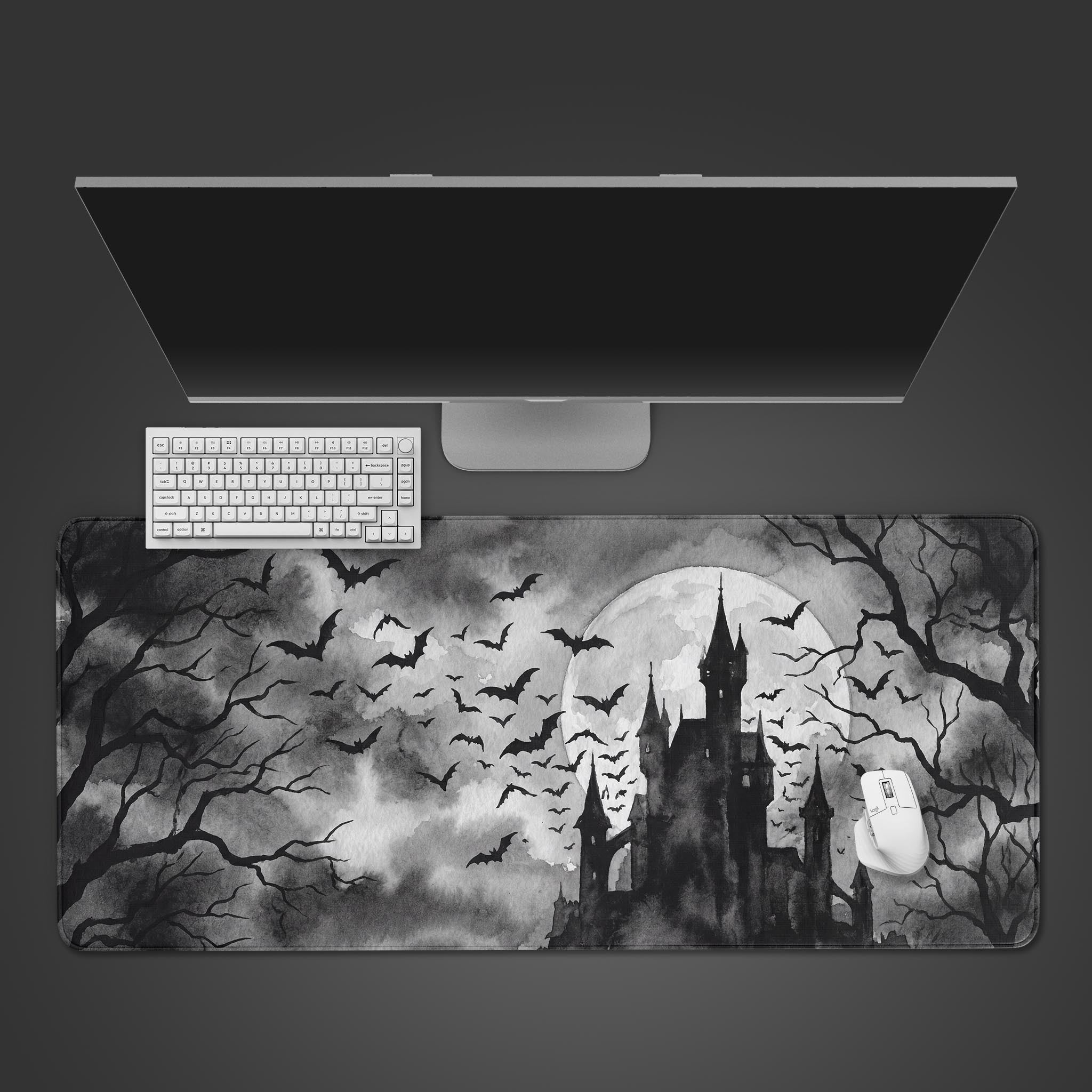 Top-down view of the Shadowed Manor gaming desk mat, featuring a gothic castle and bats, with a white keyboard and mouse on a dark gray surface. - Epic Design Pads & Mousepads