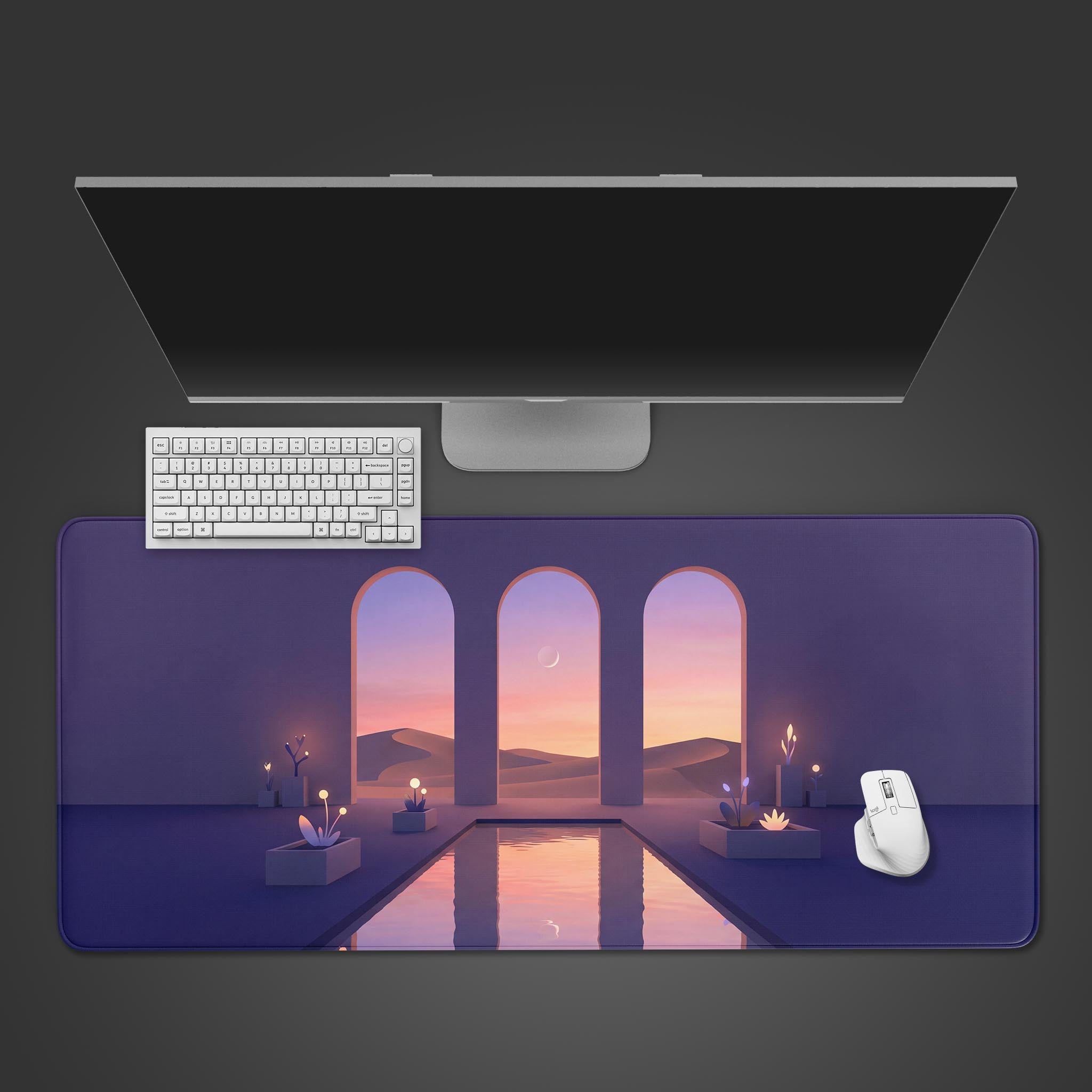 Top-down view of the Silent Archway gaming desk mat. The surreal desert landscape design is shown with a white keyboard, mouse, and a large monitor on a dark background. - Epic Design Pads & Mousepads