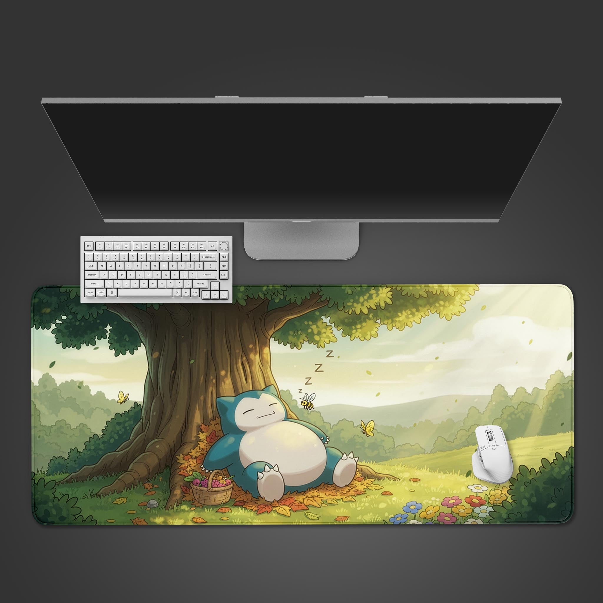 Desk setup with a large mouse pad featuring the snorlax poekemon under a tree, keyboard, and monitor on a dark background.
