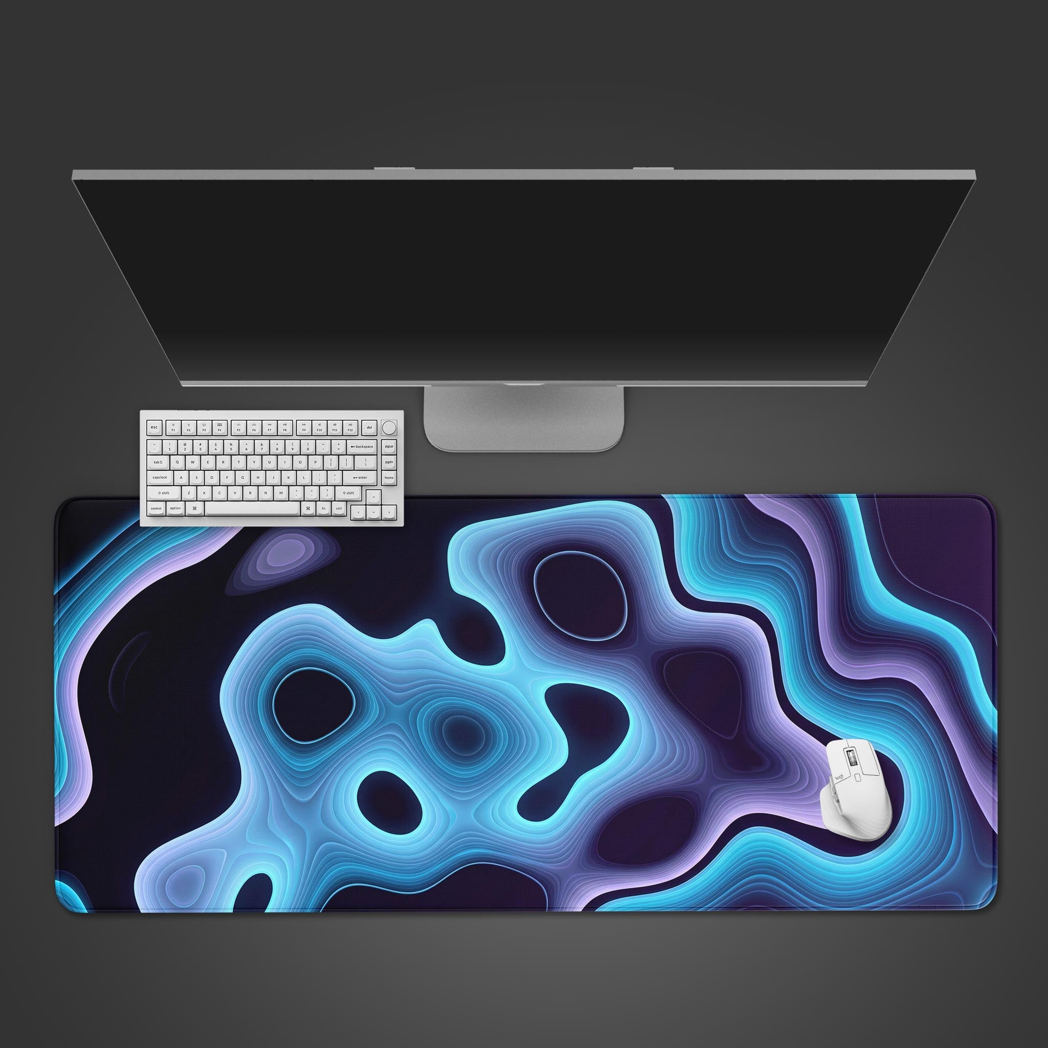 Top-down view of the Sonic Depth gaming desk mat, showcasing its abstract blue and purple wave design underneath a white keyboard, mouse, and monitor. - Epic Design Pads & Mousepads